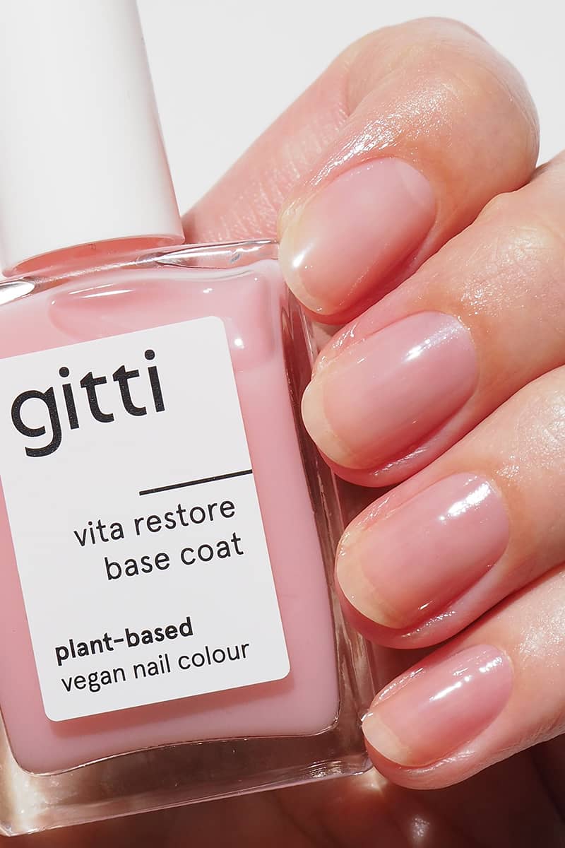 Eine Hand mit Naturnägeln, die mit Glasnagelfeile und Nagelöl präpariert sind, hält eine Flasche Soap Nails Essentials M, einen rosafarbenen veganen Nagellack auf Pflanzenbasis.