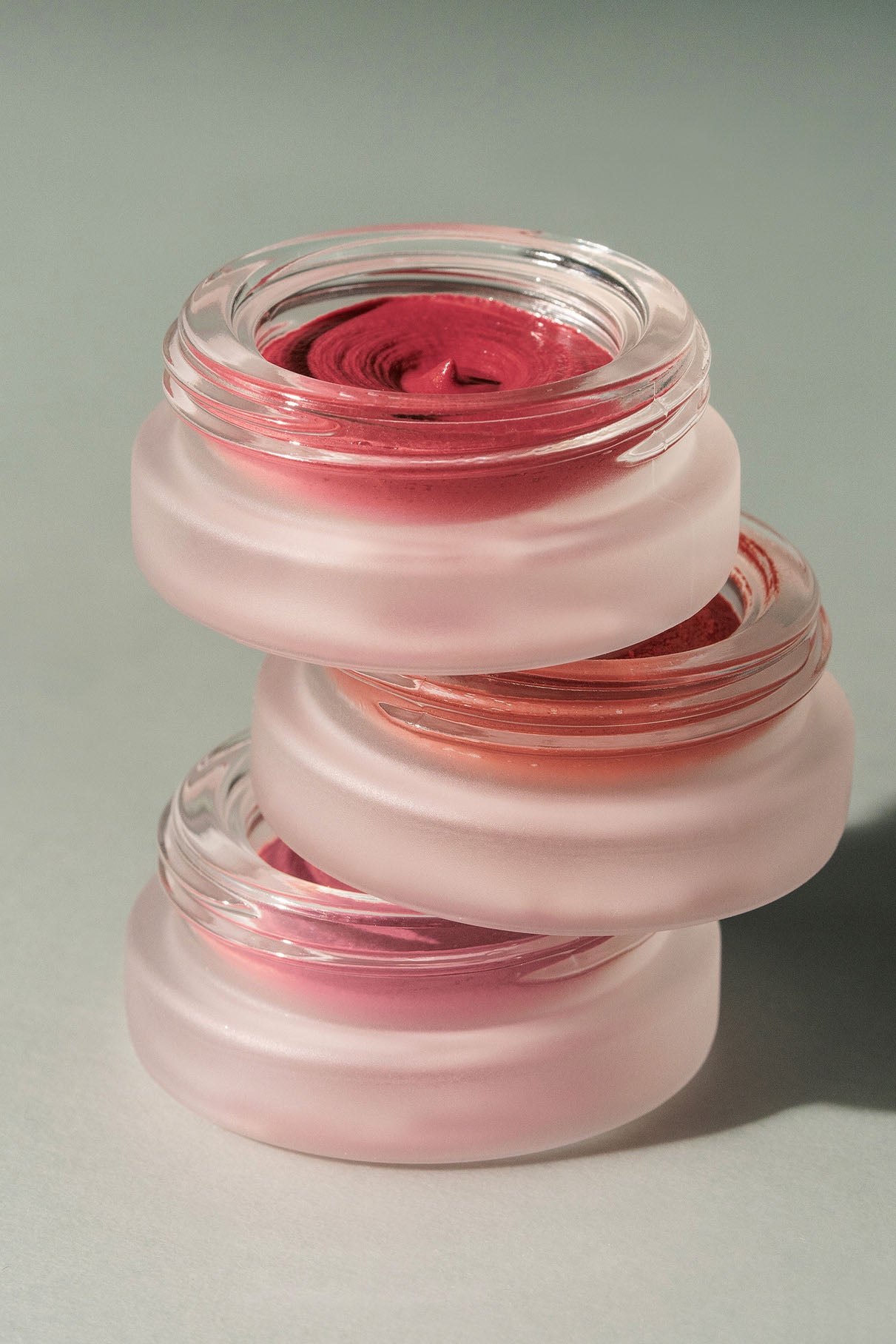 Drei runde Glasbehälter aus dem Signature Set, gefüllt mit verschiedenen Schattierungen von Lip Glaze und Velvet Cheeks Creme Make-up, sind vor einem neutralen Hintergrund übereinander gestapelt.