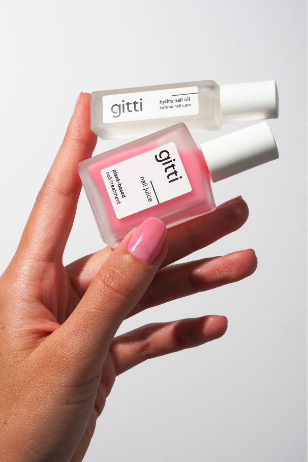 Eine Hand mit rosa lackierten Nägeln hält das Hydra & Juice Duo: einen rosa Nagellack von Gitti und ein klares Hydra-Nagelöl vor einem schlichten weißen Hintergrund.