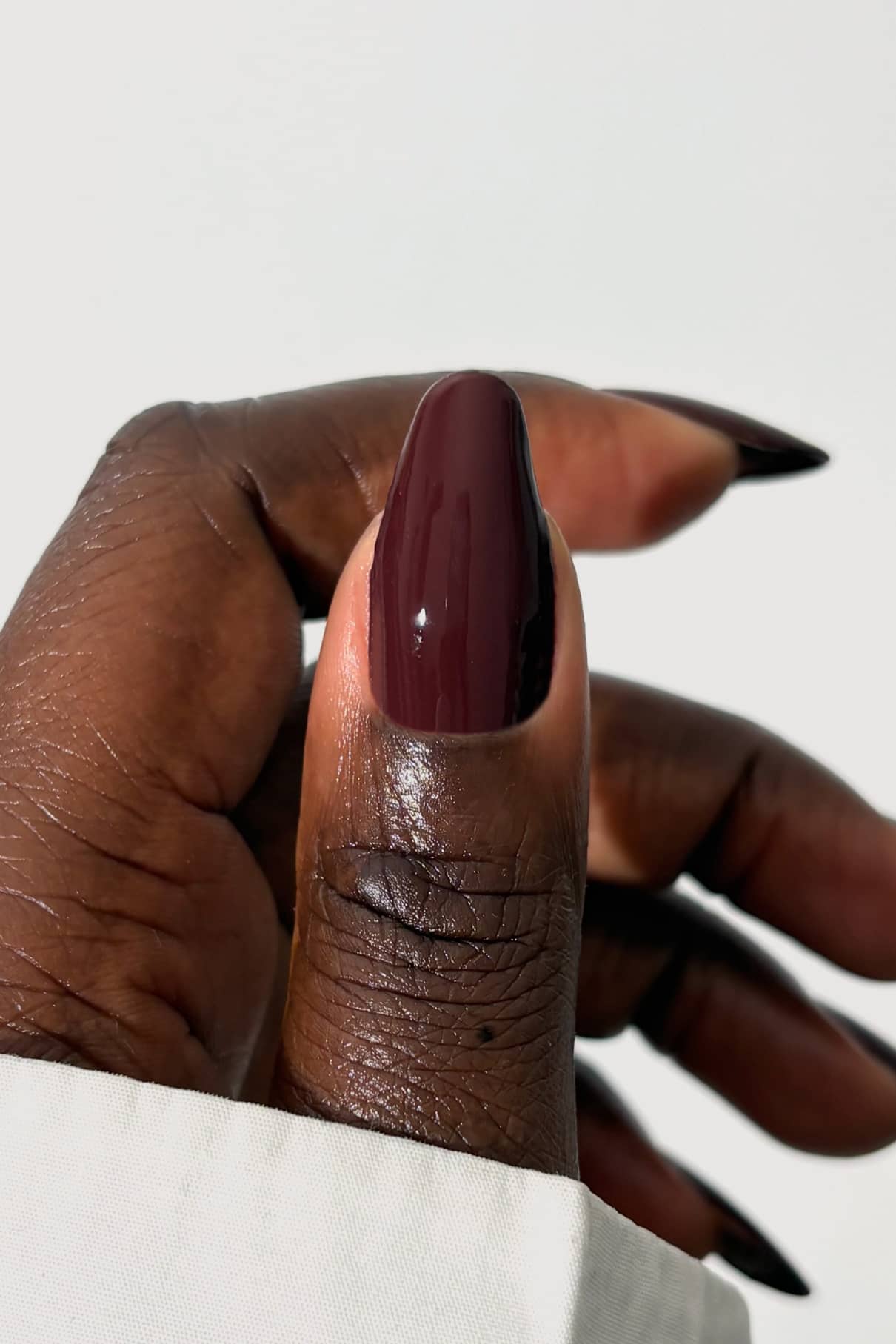 Eine Nahaufnahme einer dunkelhäutigen Hand mit langen Nägeln, die in glänzendem Burgunderrot gitti no. 055, strahlt die Eleganz aus, langsam an einem Espresso Martini zu nippen.