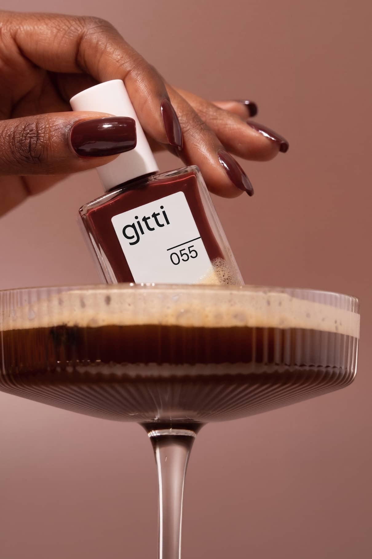 Eine Hand mit polierten Nägeln hält eine Flasche gitti no. 055 über einem Glas Espresso-Martini und lädt zum langsamen Nippen vor neutralem Hintergrund ein.