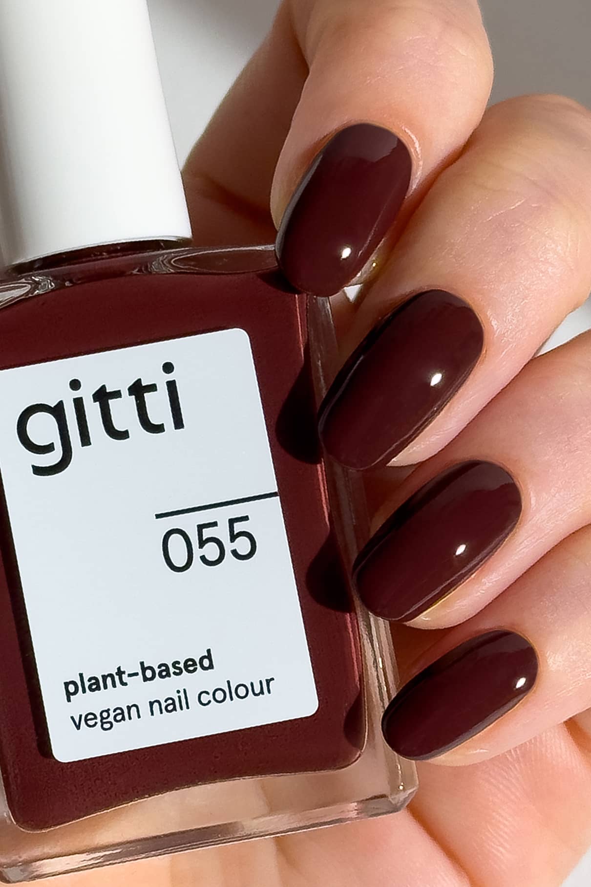 Eine Hand mit dunkelkastanienbraunen, Espresso-Martini-inspirierten Nägeln hält eine Flasche gitti no. 055 pflanzliche, vegane Nagelfarbe - ideal für alle, die gerne langsam an ihrem Stil nippen.