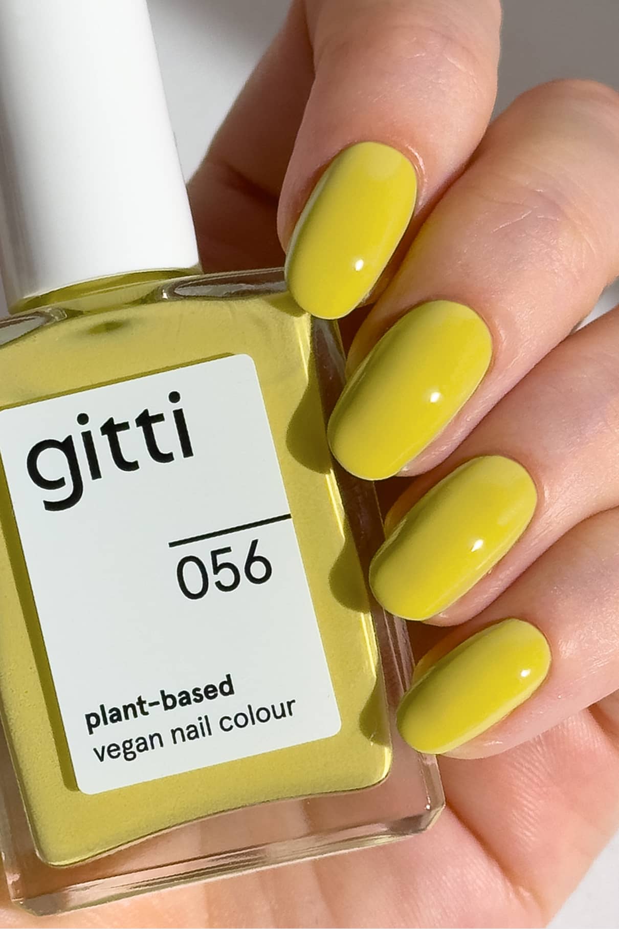 Eine Hand mit Sonnengelb polierten Nägeln hält eine Flasche gitti no. 056, eine pflanzliche, vegane Nagelfarbe in leuchtendem Gelb, die an die Helligkeit von Zitrus und die Frische eines Salzrandes erinnert.