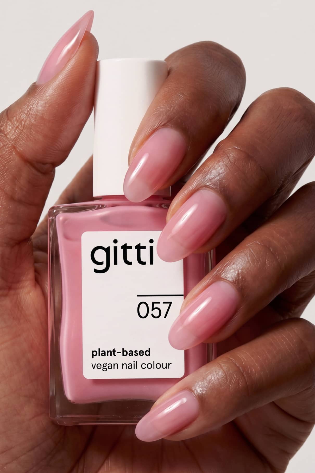 Eine Hand mit langen, manikürten Nägeln, die rosa lackiert sind, hält eine Flasche mit gitti no. 057 Nagelfarbe.