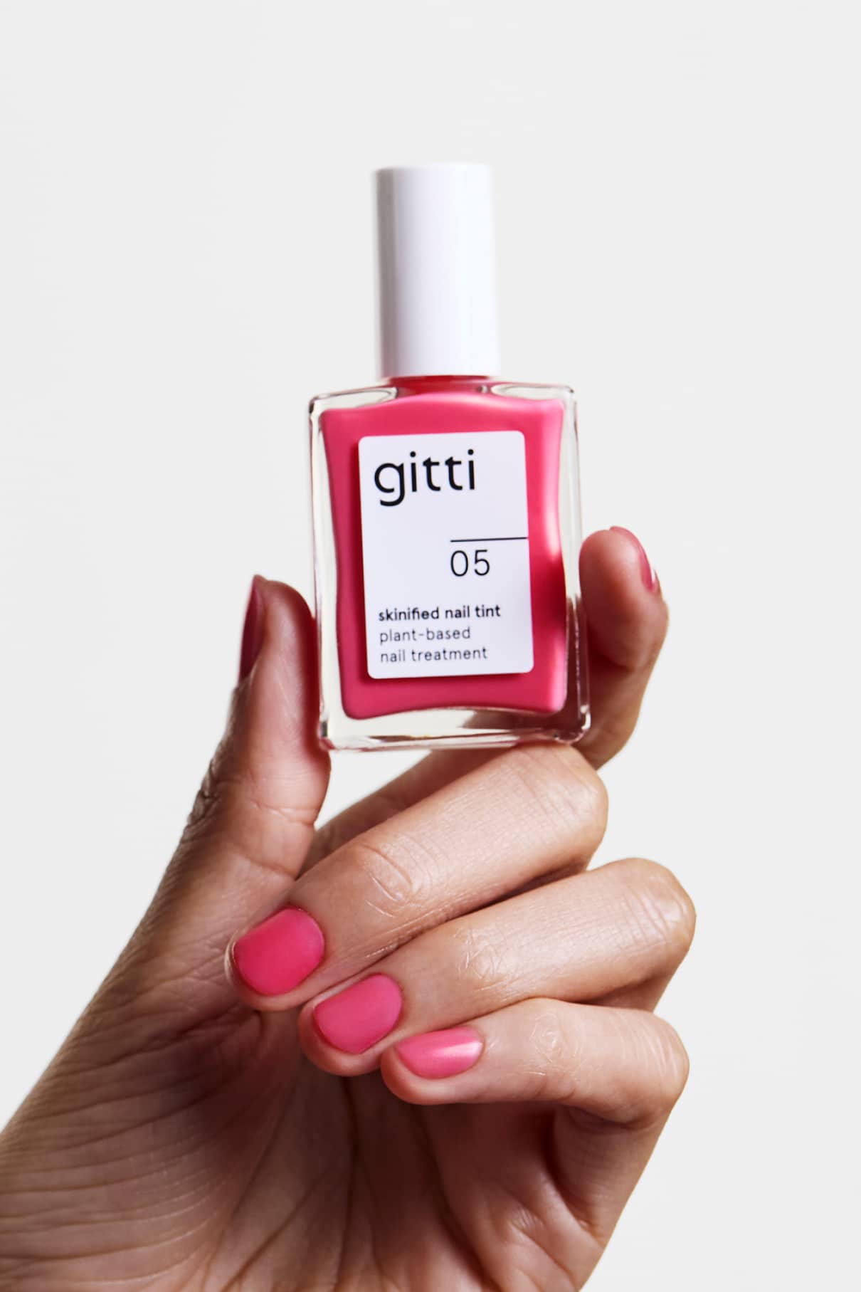 Eine Hand hält eine Flasche Skinified Nail Tint 05, die Nägel sind im gleichen Rosaton lackiert wie der pflanzliche Nagellack.
