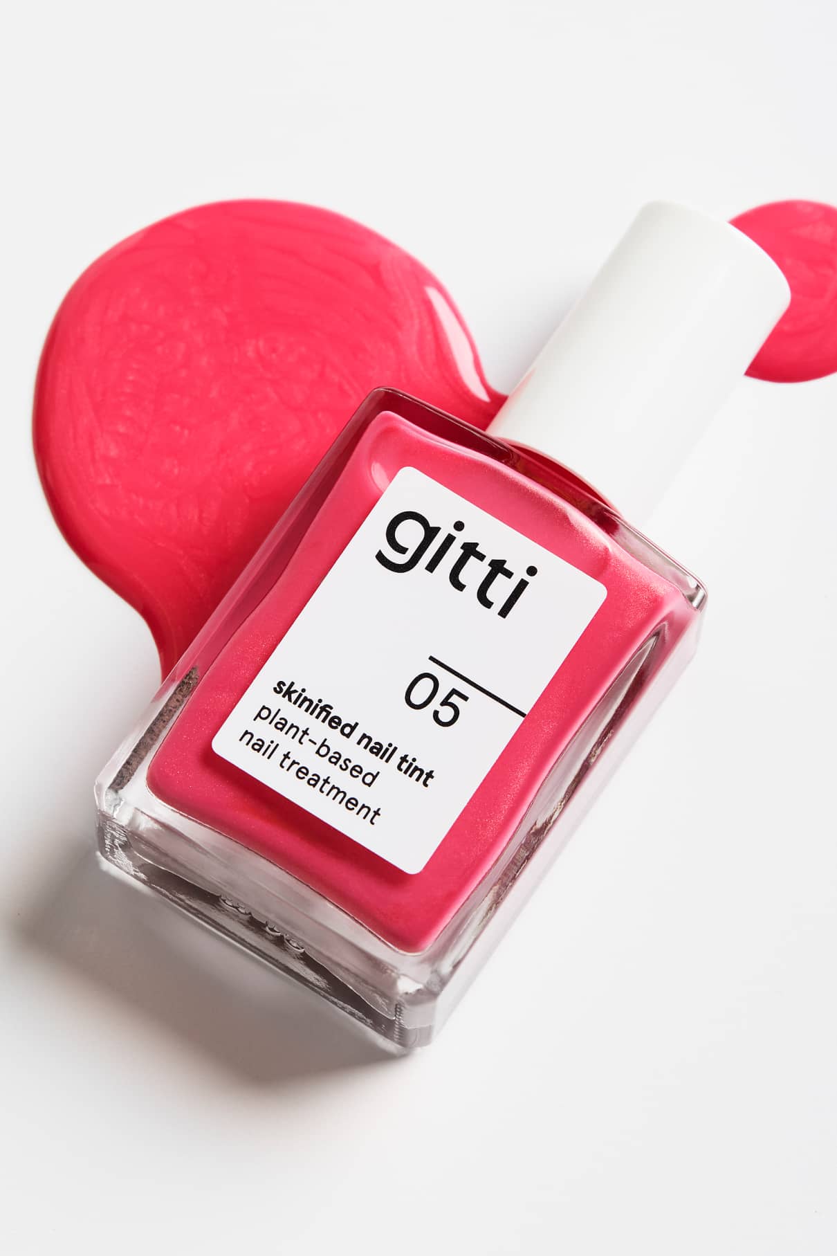 Eine Flasche Skinified Nail Tint 05 Nagelpflege mit Hyaluronsäure liegt auf der Seite, darunter und daneben ist leuchtend rosa Nagelfarbe verschüttet.