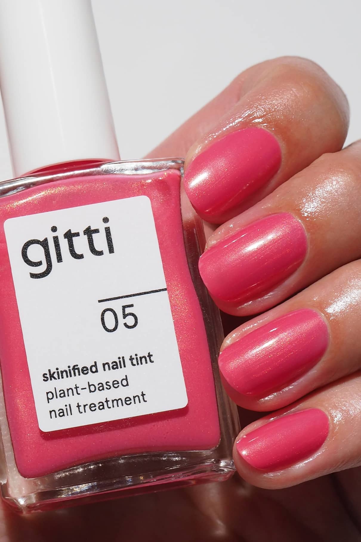 Eine Hand mit in glänzendem rosa Pflegelack lackierten Nägeln hält eine Flasche mit der Aufschrift Skinified Nail Tint 05, eine pflanzliche Nagelpflege mit Hyaluronsäure.