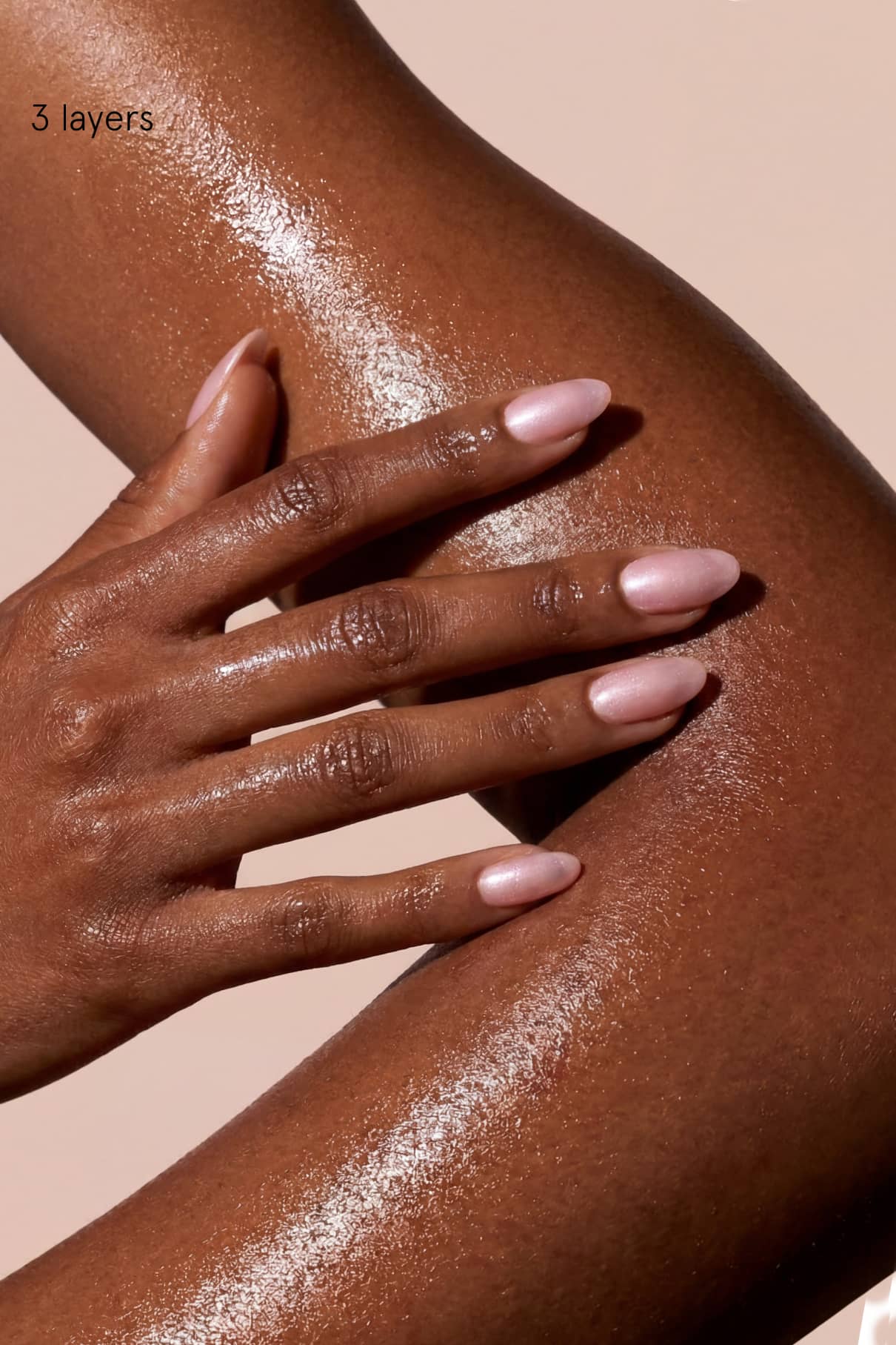 Eine Hand mit hellrosa Skinified Nail Tint 08 polierten Nägeln ruht auf einem glänzenden, befeuchteten Unterarm mit glatter brauner Haut. Der Text lautet "3 Schichten".