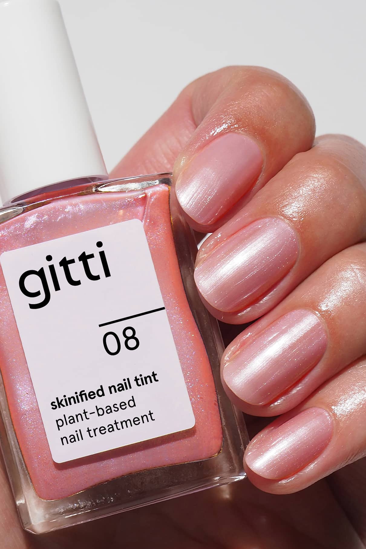 Eine Hand mit glänzenden, hellrosa Nägeln hält eine Flasche Skinified Nail Tint 08, eine mit Vitamin C angereicherte Nagelpflege auf Pflanzenbasis.