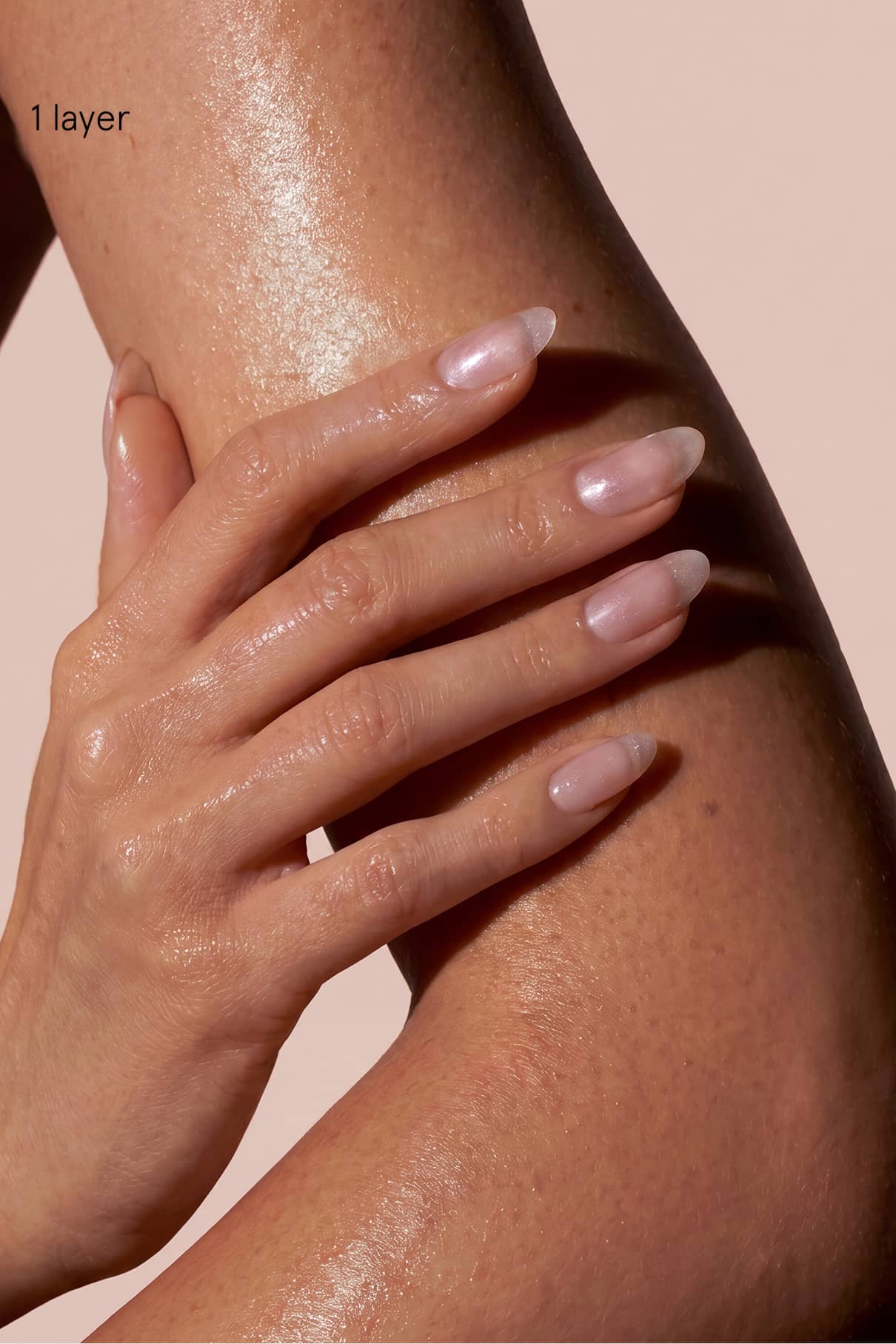 Eine Nahaufnahme einer Hand mit manikürten Nägeln, die mit Skinified Nail Tint 09 lackiert sind, ruht auf einem befeuchteten, glänzenden Arm. Der Text "1 Schicht" erscheint in der oberen linken Ecke.