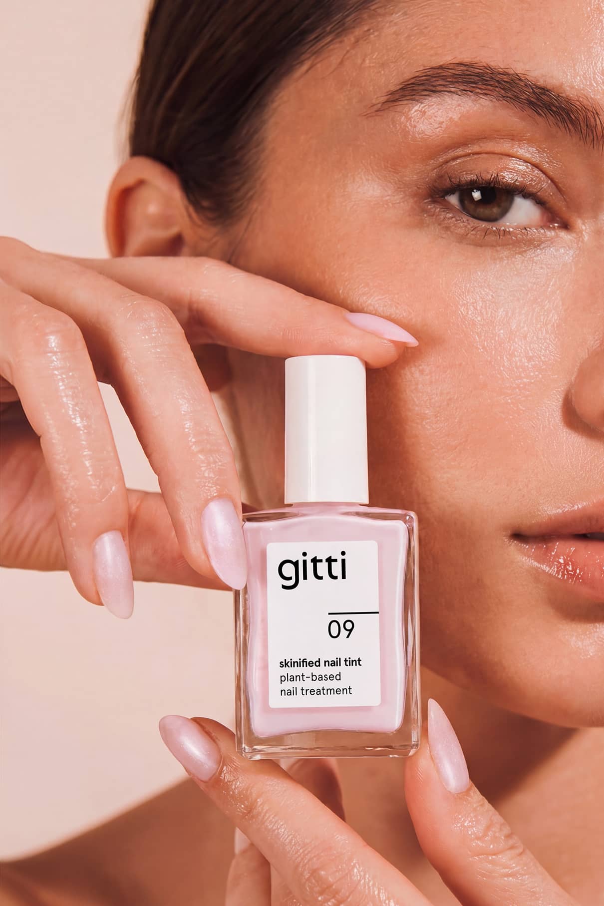 Eine Person hält eine Flasche Skinified Nail Tint 09 in der Hand und zeigt ihre lackierten Nägel in der Nähe ihres Gesichts.