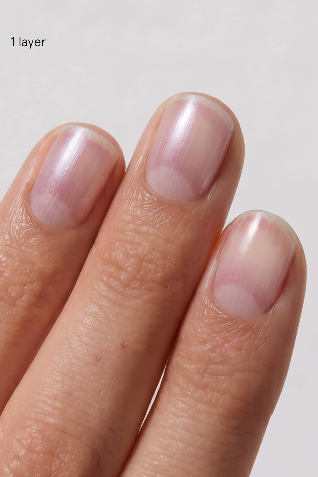 Nahaufnahme von drei Fingernägeln mit einer einzigen Schicht Skinified Nail Tint 09 mit Hyaluronsäure in hellem Rosa. Der Text "1 Schicht" wird in der oberen linken Ecke angezeigt.