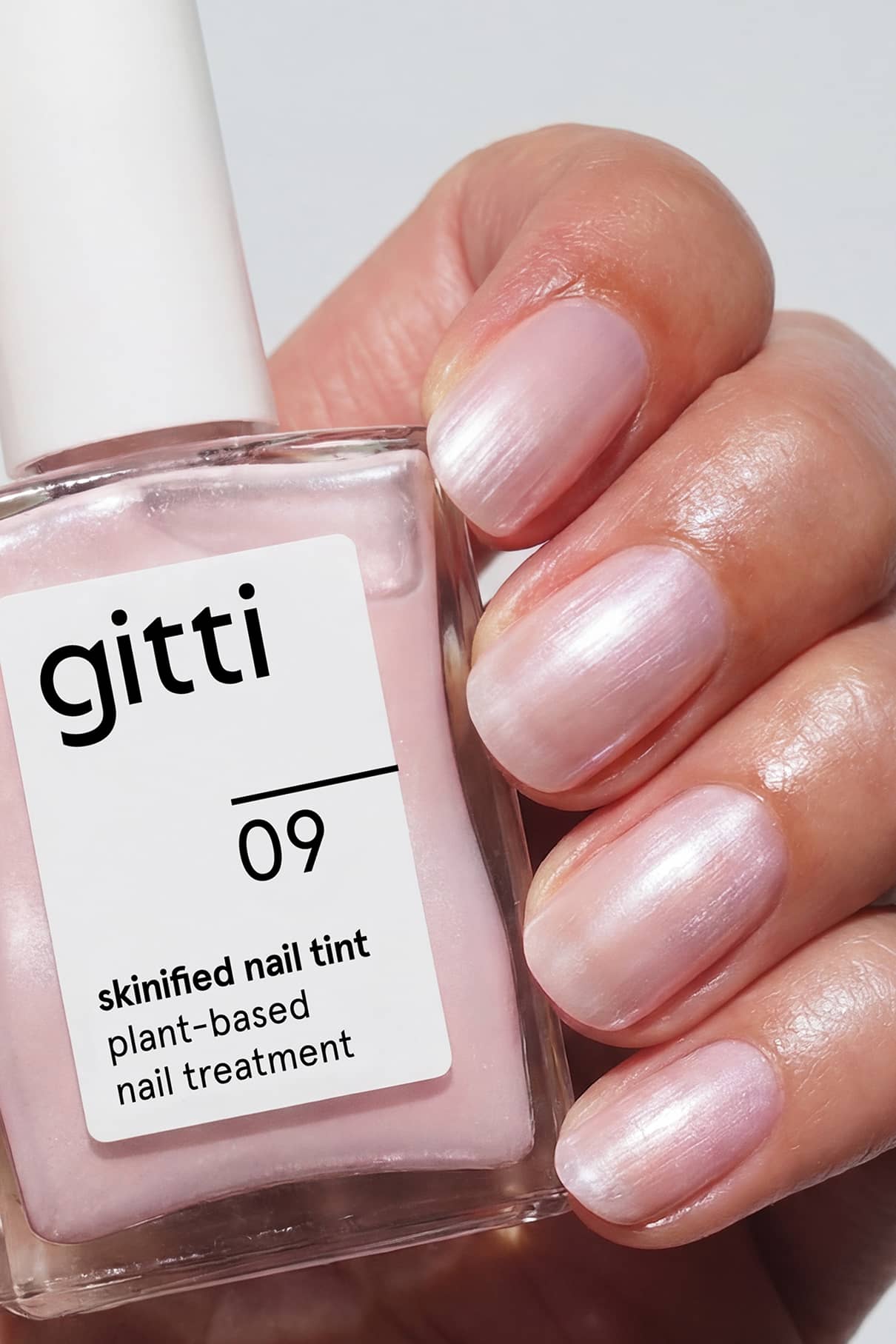 Eine Hand mit sauber manikürten Nägeln, die in einem hellen Rosa lackiert sind, hält ein Fläschchen mit der Aufschrift Skinified Nail Tint 09, eine pflanzliche Nagelbehandlung, die mit Hyaluronsäure angereichert ist und zusätzliche Feuchtigkeit spendet.