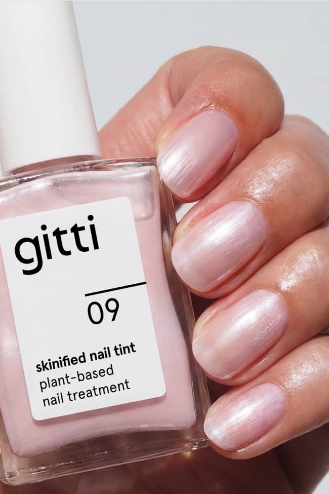 Eine Hand mit polierten Nägeln hält ein 15-ml-Fläschchen von gitti 09 skinified nail tint, einer pflanzlichen Nagelpflege aus dem innovativen Treatment Duo Set.
