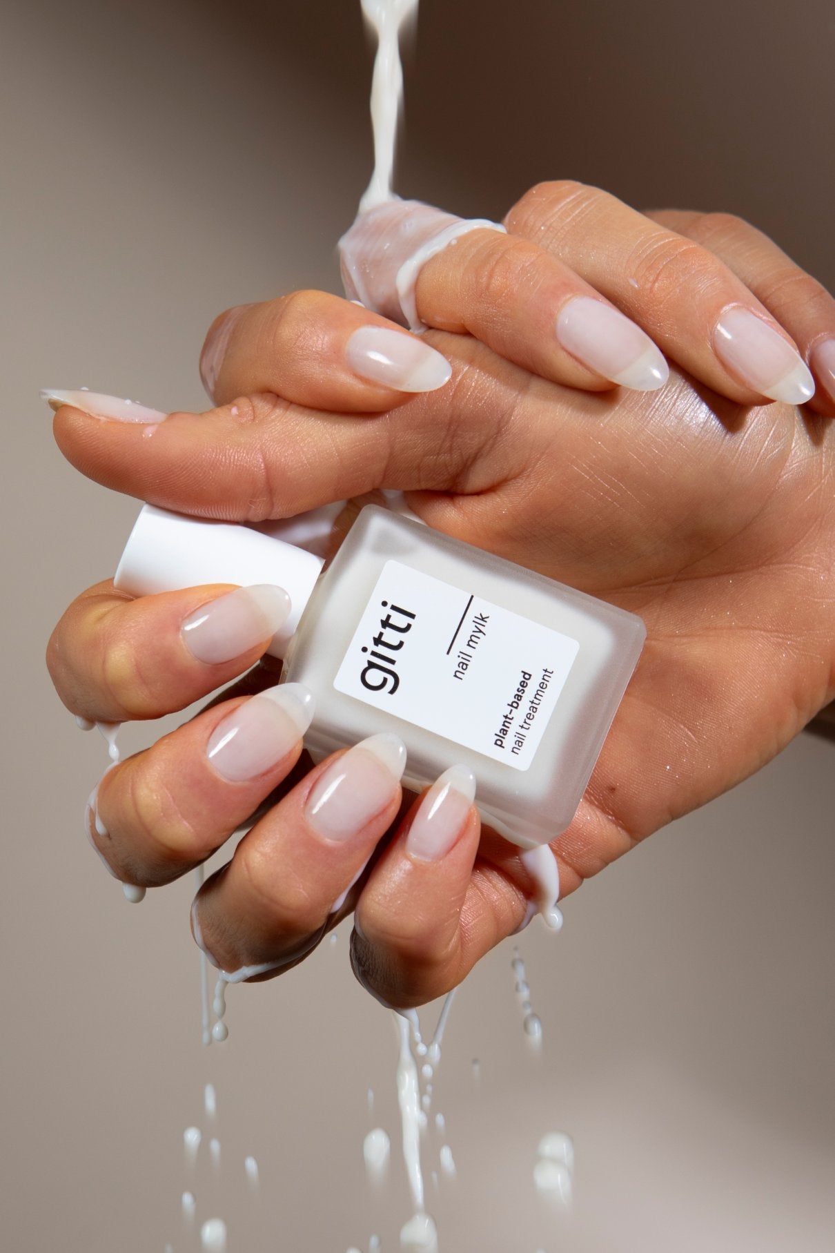 Eine Hand mit manikürten Nägeln hält das Perfect Nails Starter Set, während sich eine milchige Flüssigkeit darüber ergießt, die das glänzende Finish hervorhebt - eine ideale Ergänzung für Ihre Nagelpflege-Routine.