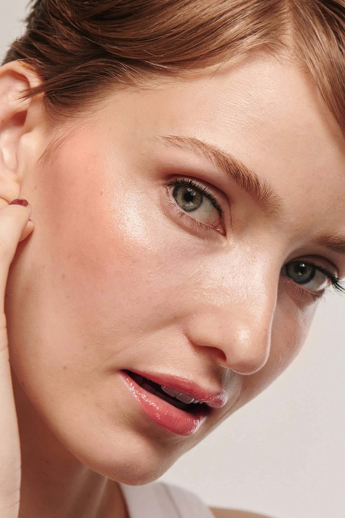 Nahaufnahme einer Person mit heller Haut, grünen Augen und hellbraunem Haar, die ihre Wange berührt und zur Seite schaut, wobei ein dezenter Fresh Up Set Highlighter für einen strahlenden, aber natürlichen Glanz sorgt.