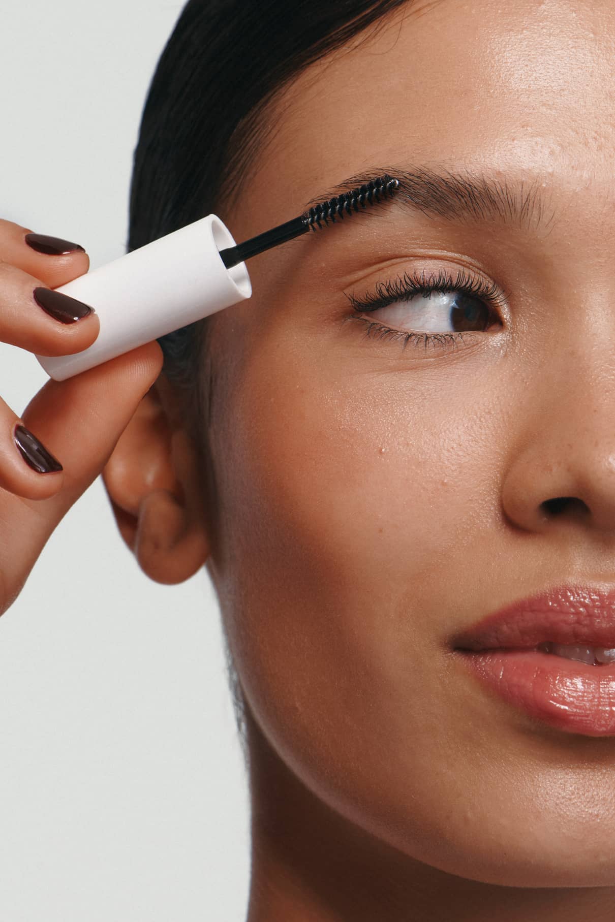 Eine Person verwendet Brow Control mit einem Spoolie-Pinsel, um ihre Augenbraue zu formen. Die Nahaufnahme zeigt nur die Hälfte des Gesichts und hebt die nicht-klebrige, leichte Textur des transparenten Gels hervor.