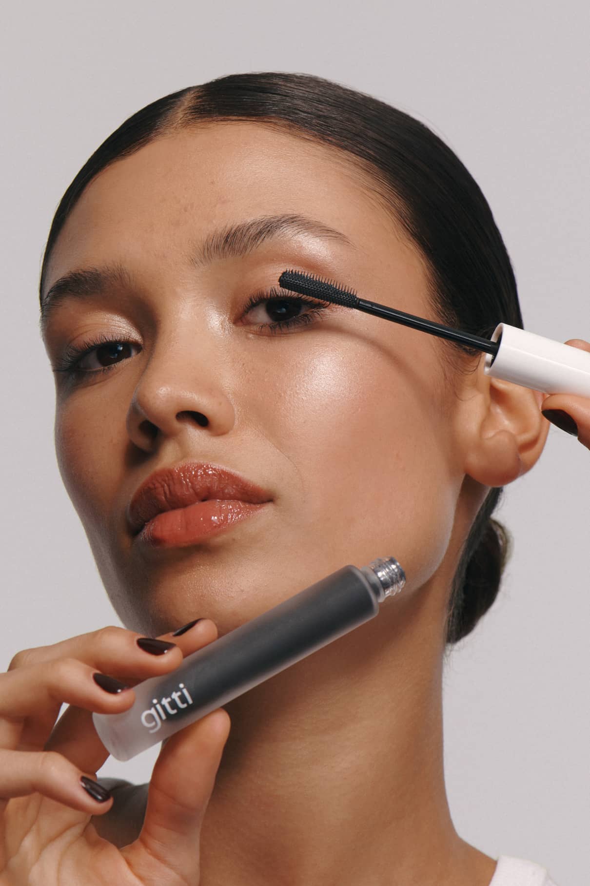 Eine Person mit glatter Haut trägt Infinite Lash mit einer schwarz-weißen Tube mit der Aufschrift gitti auf ihre oberen Wimpern auf, um sie zu definieren und zu verlängern.