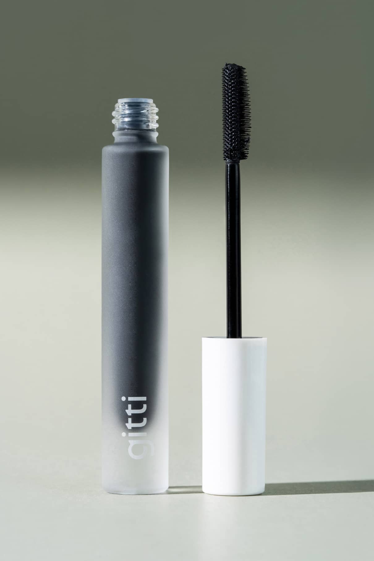 Eine Mascara-Tube mit schwarzem Bürstenstab und weißer Kappe steht aufrecht neben dem mattgrauen Behälter mit der Aufschrift gitti - eine unverzichtbare Ergänzung für jedes Lash Duo-Set.