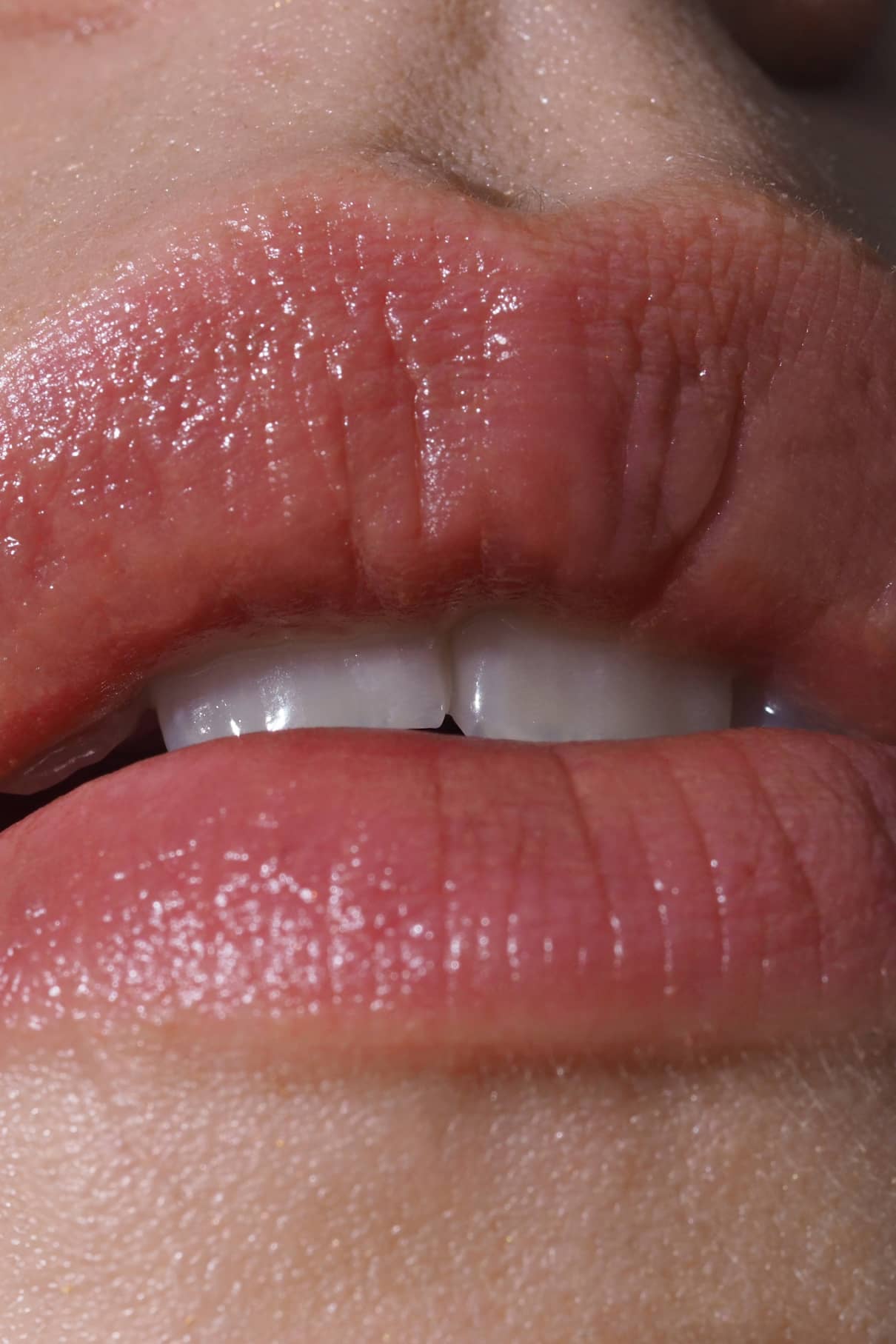 Nahaufnahme von Lippen und oberen Zähnen, die Lip Sync Refill Nr. 01, mit natürlichem Hautton mit rötlichem Unterton und Lichtreflexionen auf den feuchten Lippen.