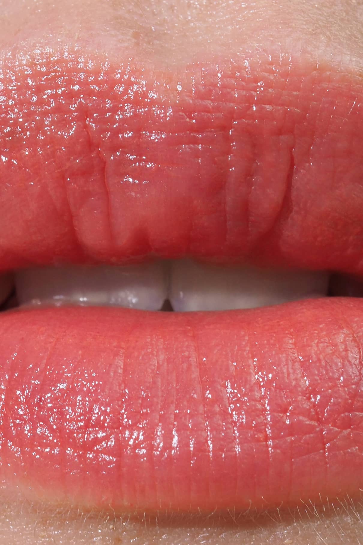 Nahaufnahme von Lippen in einem rosa Korallton, leicht glänzend und mit sichtbaren oberen Zähnen - perfekt für warme und neutrale Hauttypen. Getragen wird Lip Sync Refill no. 03.