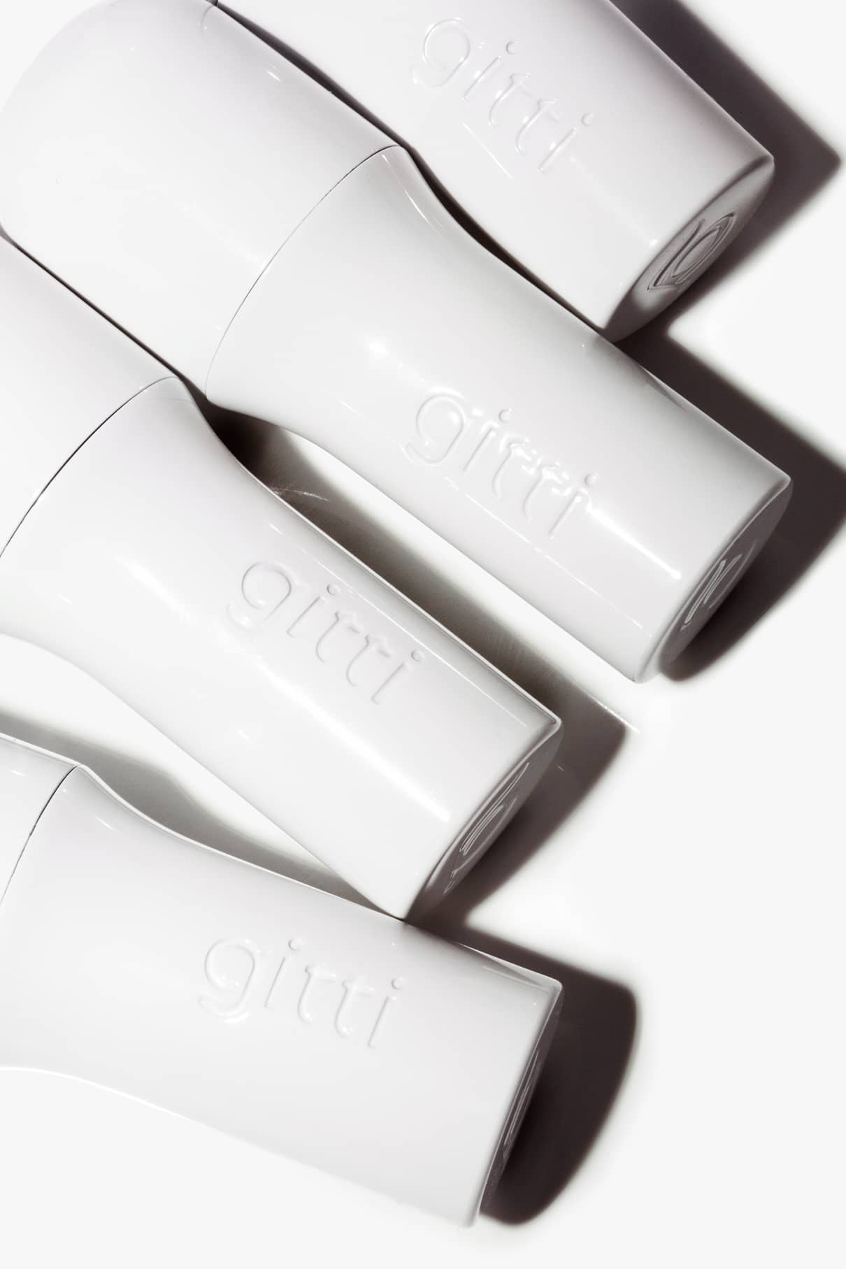 Vier weiße, zylindrische Flaschen mit der Prägung "gitti" sind diagonal auf weißem Hintergrund angeordnet und mit einer haltbaren, nachfüllbaren Hülle versehen, die vom innovativen Design des Lip Sync Case inspiriert ist.