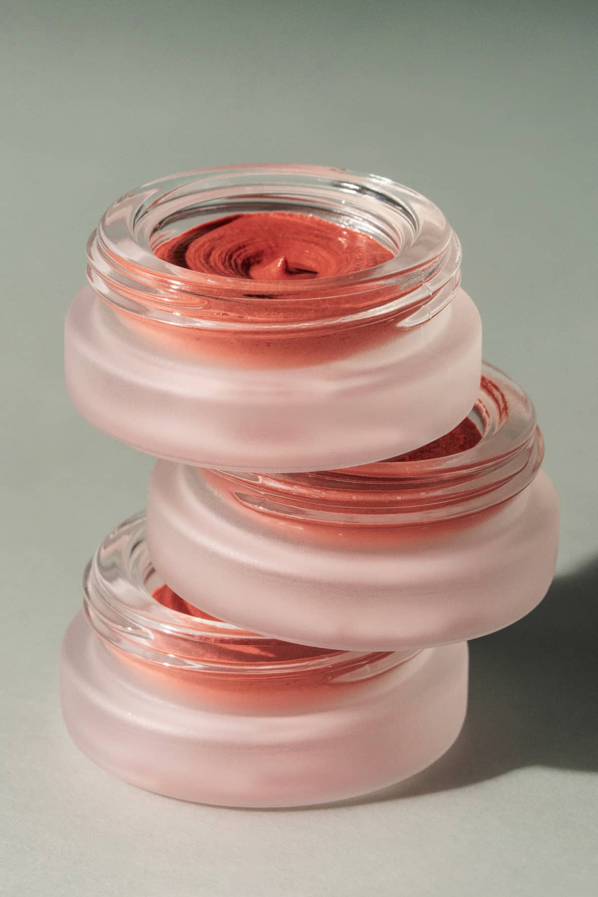 Drei mit rötlich-brauner Creme gefüllte Tiegel aus Milchglas sind ordentlich gestapelt und präsentieren das luxuriöse Lip & Cheek Duo vor einem neutralen Hintergrund.