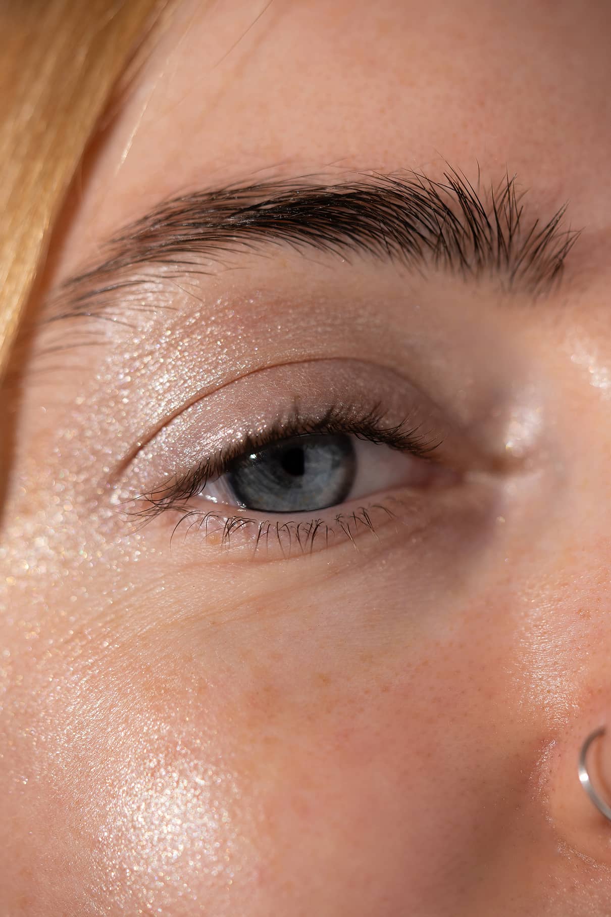 Nahaufnahme des blauen Auges einer Person, das mit Visionist Nr. 05 hervorgehoben wurde, mit Augenbraue, einem Teil der Nase mit silbernem Nasenring und detaillierter Hauttextur.