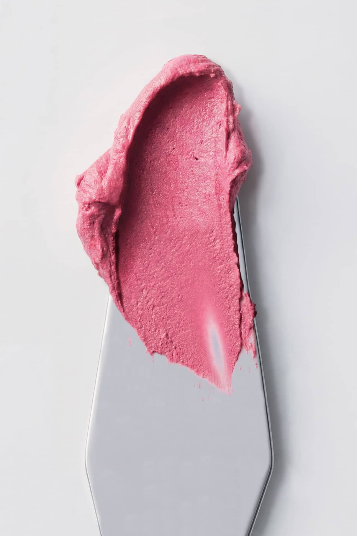Ein Klecks Velvet Cheeks no. 05 silikonfreies Mousse-Blush in kräftigem Pink ruht auf einem Metallspatel vor einem weißen Hintergrund.