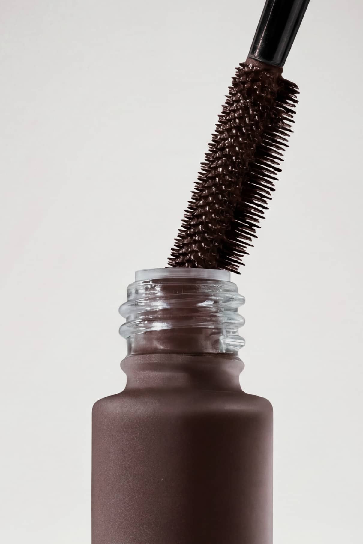 Eine Nahaufnahme des Infinite Lash Nr. 02 Mascarastifts, der aus einer mattbraunen Tube gezogen wird, vor einem schlichten weißen Hintergrund.