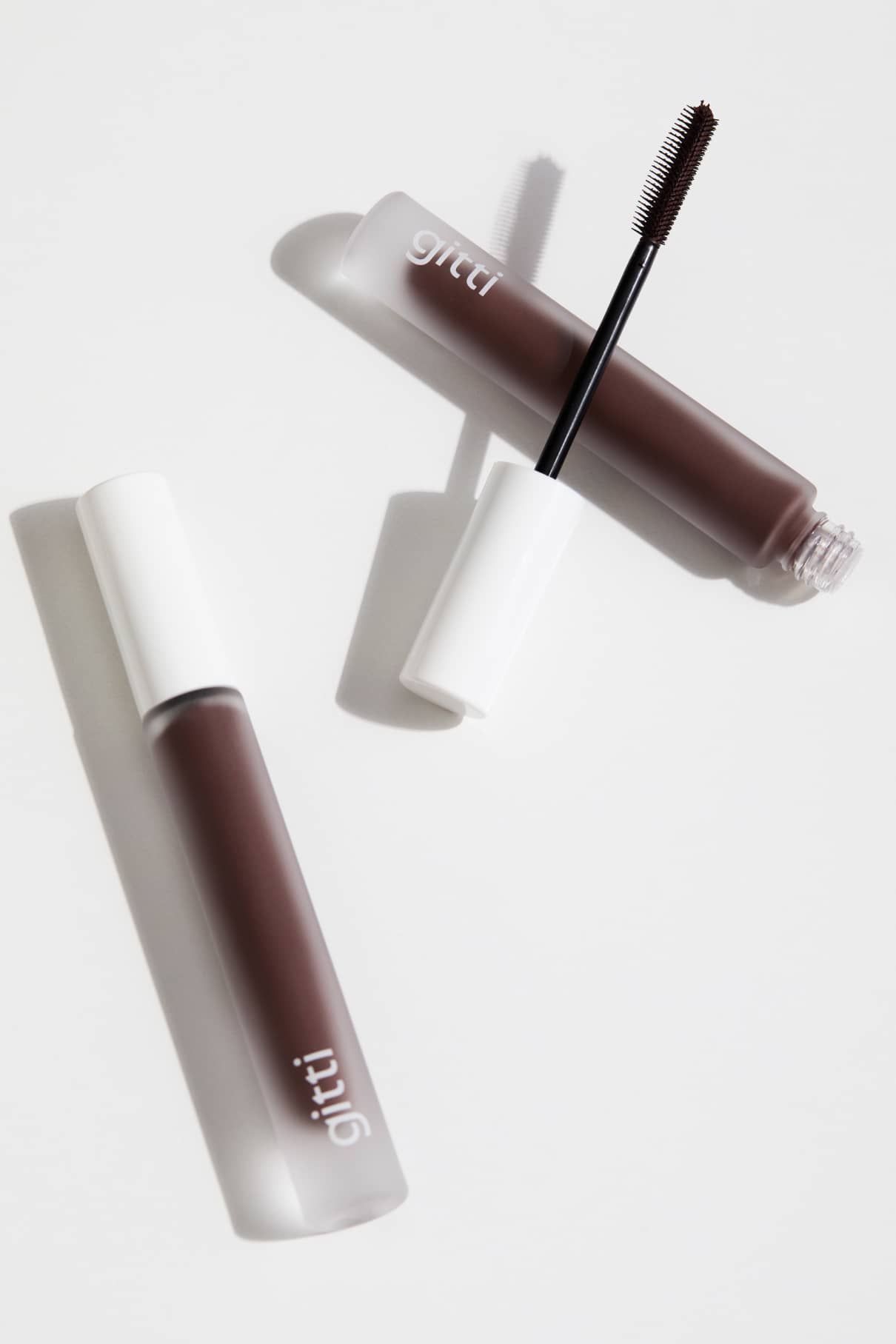 Zwei Tuben Infinite Lash Nr. 02 Mascara, beide mit weißen Kappen - eine davon geöffnet, um den präzisen Bürstenapplikator zu zeigen - sind vor einem weißen Hintergrund abgebildet.