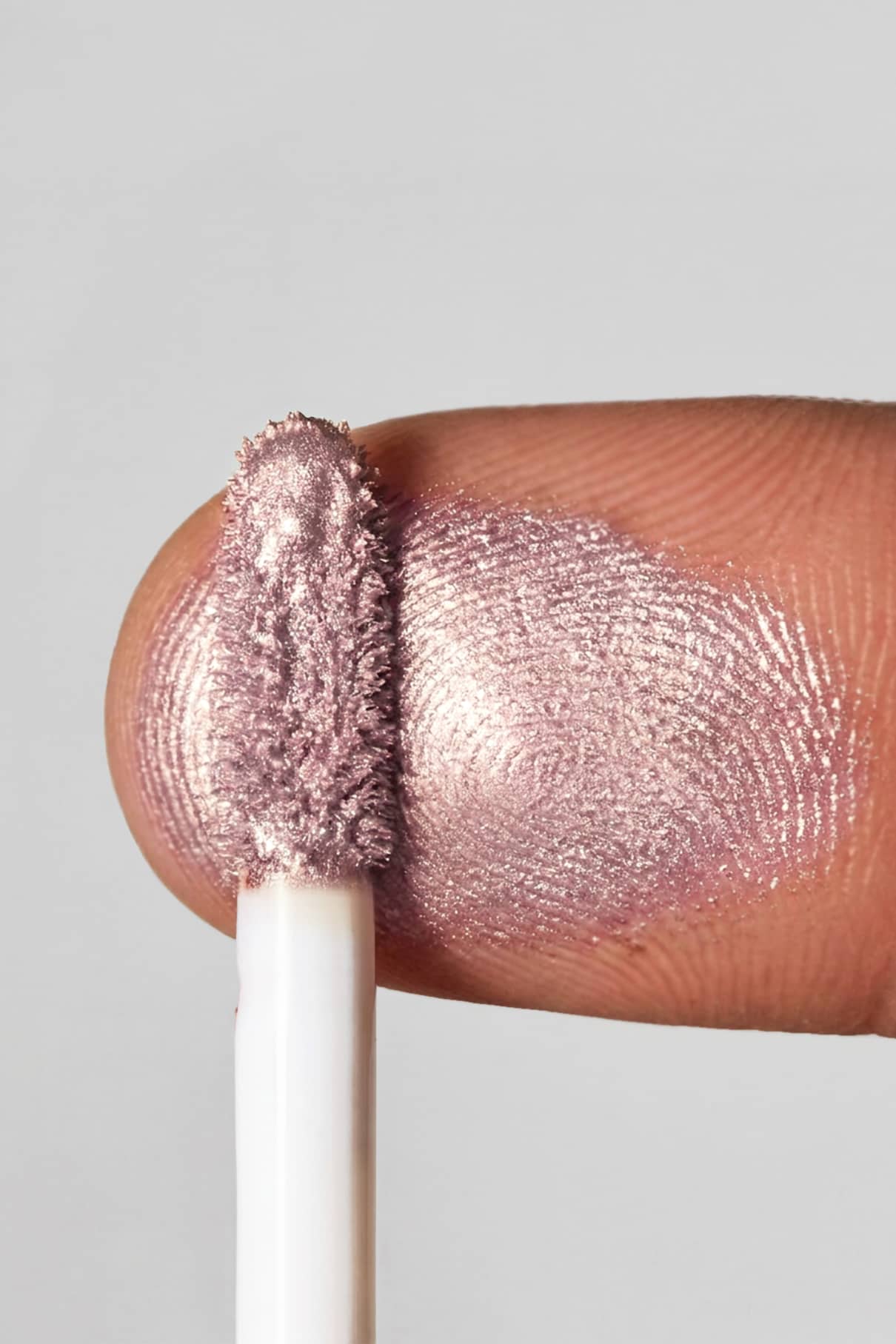 Nahaufnahme eines Fingers, der mit dem metallisch rosa schimmernden Halo Eyes no. 04 Lidschatten, als ein weißer Applikator die lichtreflektierende Fingerspitze berührt.