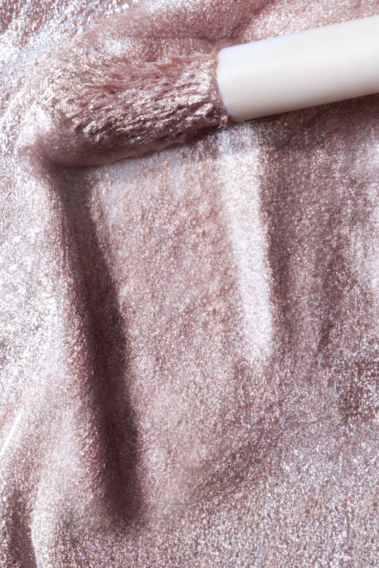 Eine Nahaufnahme zeigt einen Pinsel, der Halo Eyes no. 04, einen schimmernden roséfarbenen Metallic-Lack, auf eine Oberfläche aufträgt, wodurch ein lichtreflektierender Effekt entsteht.