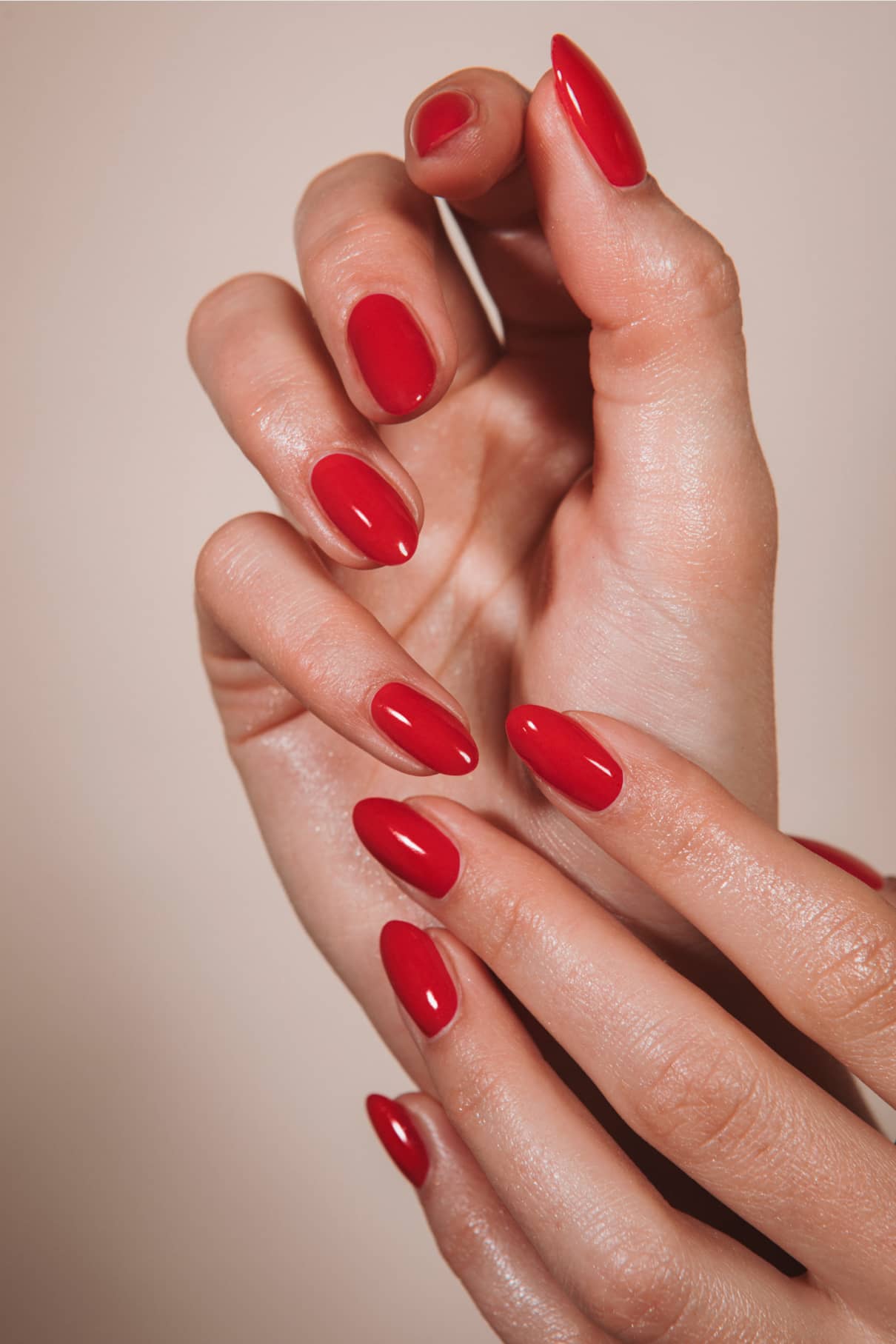 Nahaufnahme von Händen mit gepflegten Nägeln, lackiert in „Gitti x PETA“, einem leuchtenden Rot mit orangefarbenen Untertönen; die Finger berühren sich sanft vor einem neutralen Hintergrund.