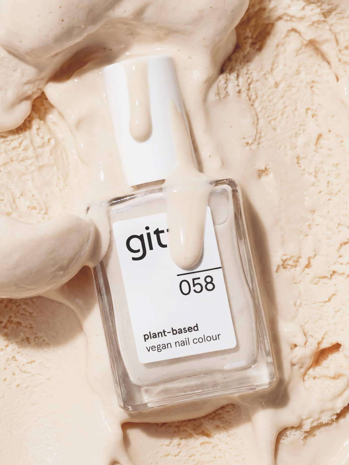 Eine Flasche des pflanzlichen, veganen Nagellacks „Gitti Nr. 058“ steht auf einer sandfarbenen, cremefarbenen, cremeartigen, cremefarbenen Oberfläche, wobei etwas von der Flüssigkeit auf die Flasche tropft, um ihr ein eleganteres Aussehen und einen wärmeren Farbton zu verleihen.
