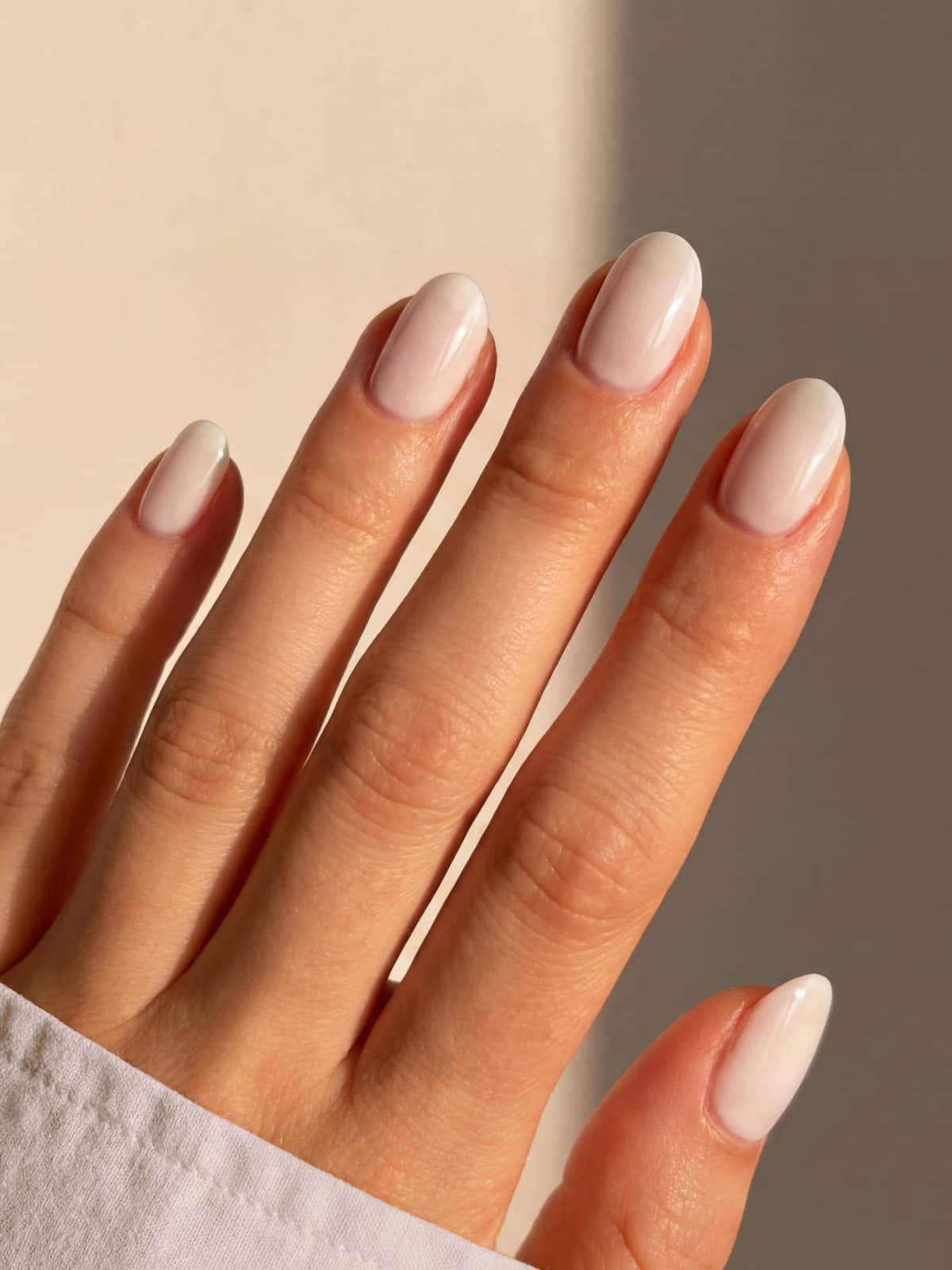 Eine Hand mit gepflegten Nägeln, lackiert in „Gitti Nr. 058“ – einem sandigen Off-White, einem hellen, glänzenden Nude-Farbton – wird vor einem neutralen Hintergrund gezeigt und sorgt so für einen eleganten Look mit einem wärmeren Farbton.