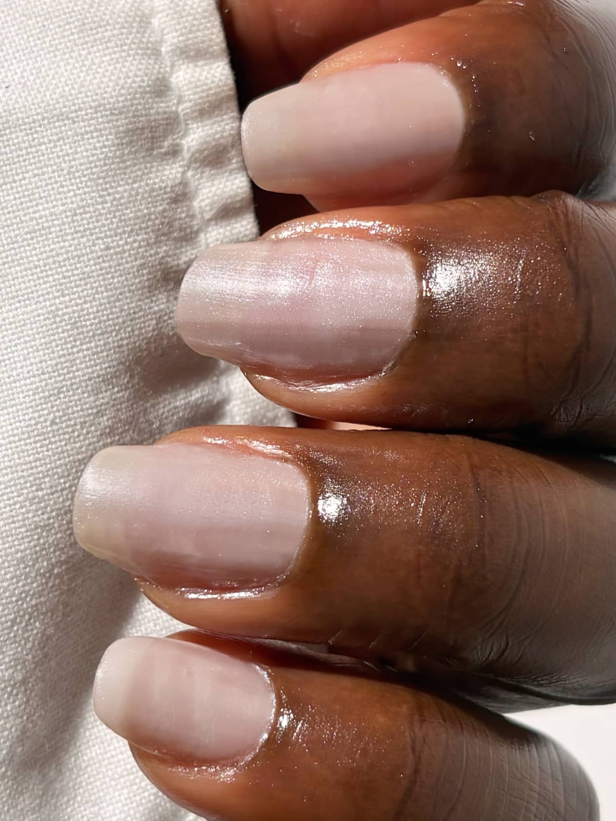Eine Nahaufnahme einer Hand mit gepflegten, natürlich aussehenden Nägeln, lackiert mit „Gitti Nr. 059“ – einem zarten Rosé-Ton –, die einen weißen, strukturierten Stoff hält, um einen strahlenden Look zu erzielen.
