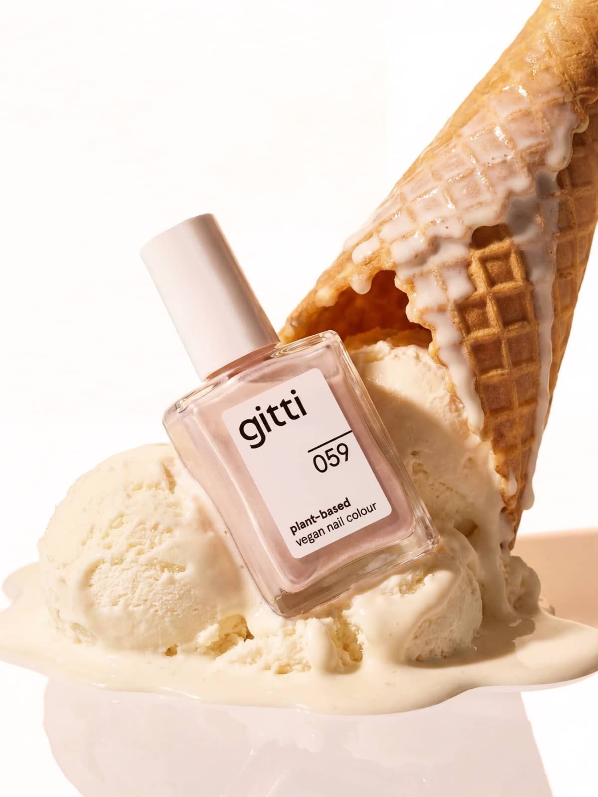 Eine Flasche „gitti no. 059“ Vegan-Nagellack in einem zarten Rosé-Ton ruht auf schmelzendem Vanilleeis, gekrönt von einer umgestürzten Waffeltüte – für einen strahlenden Look mit dezentem Schimmer.