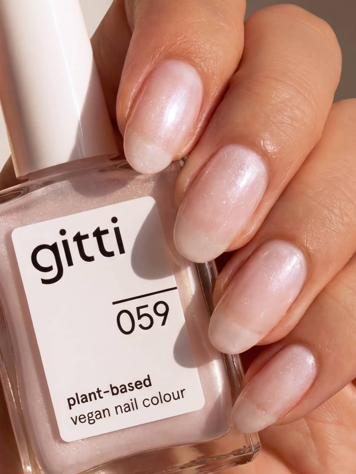 Eine Hand mit kurzen, gepflegten Nägeln, die mit einem perlmuttfarbenen, durchscheinenden Nagellack lackiert sind, hält eine Flasche aus dem „Colour & Concentrate Trio“ in der Hand und unterstreicht damit die Schönheit pflanzlicher Farben.