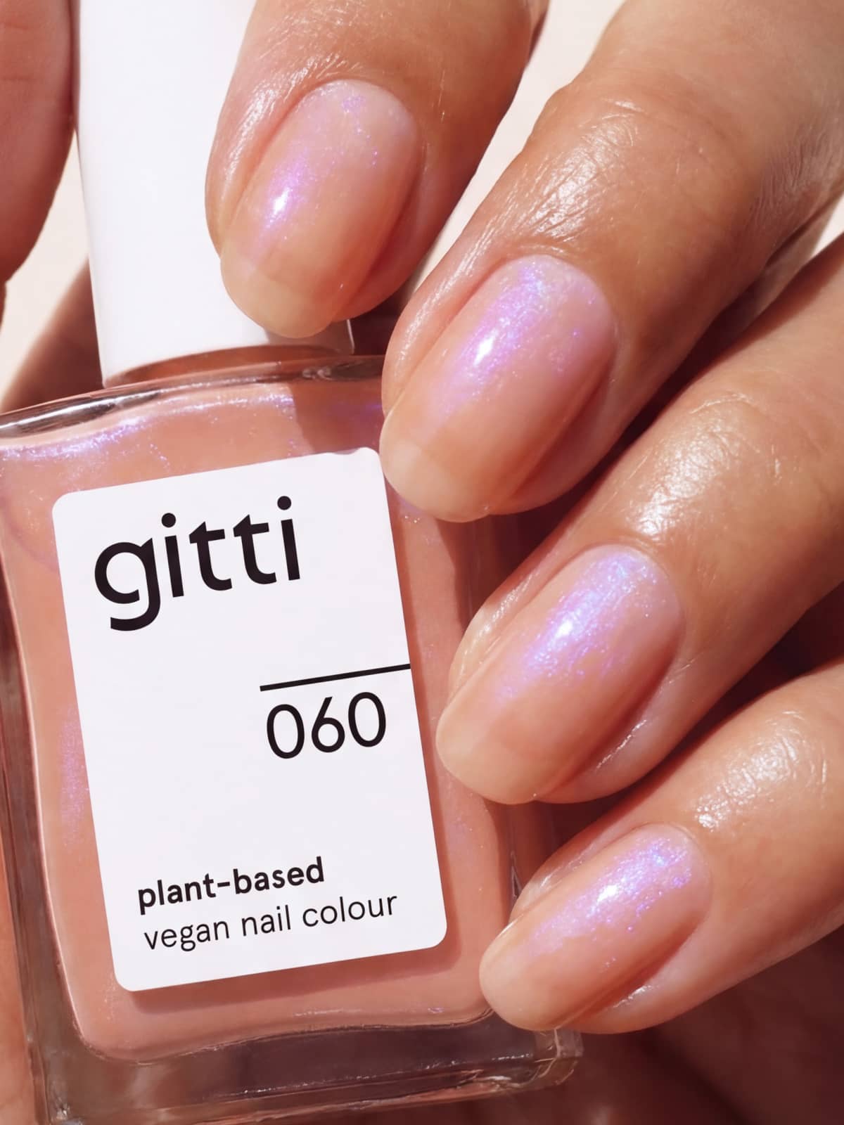 Nahaufnahme einer Hand mit schimmernden rosa Nägeln, die eine Flasche des pflanzenbasierten, veganen Nagellacks von Gitti in der Farbe 060 hält. Entdecken Sie die Schönheit pflanzenbasierter Farben und veredeln Sie Ihren Look mit dem „Colour & Concentrate Trio“ für natürlich gepflegte Nägel.