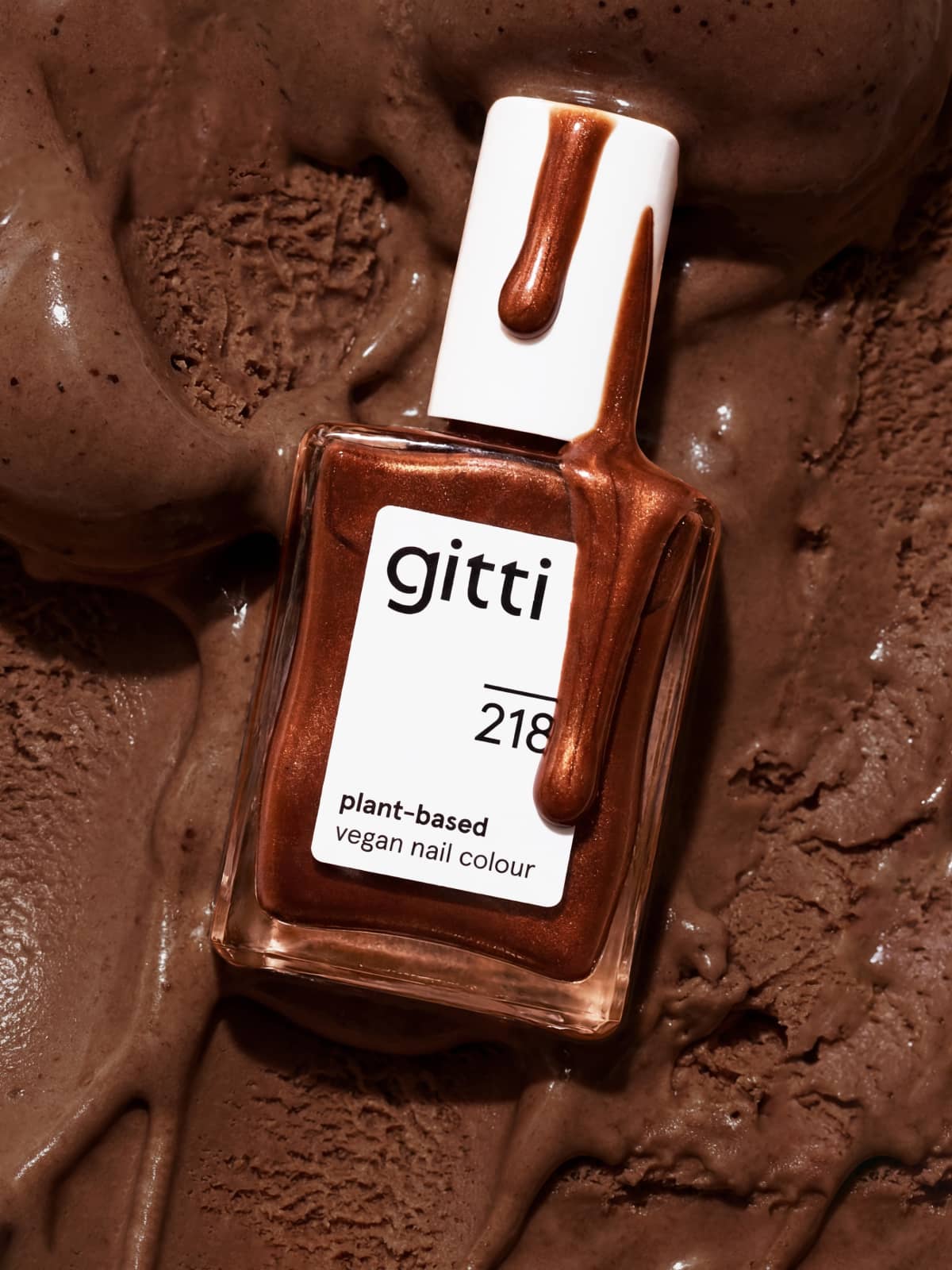 Eine Flasche des pflanzlichen, veganen Nagellacks „Gitti Nr. 218“ in der Farbe „Schokoladenbraun“ steht auf einer Kugel schmelzendem Schokoladeneis, wobei Nagellacktropfen über den Verschluss laufen und so die intensive Tiefe sowie das dezente Metallic-Finish unterstreichen.