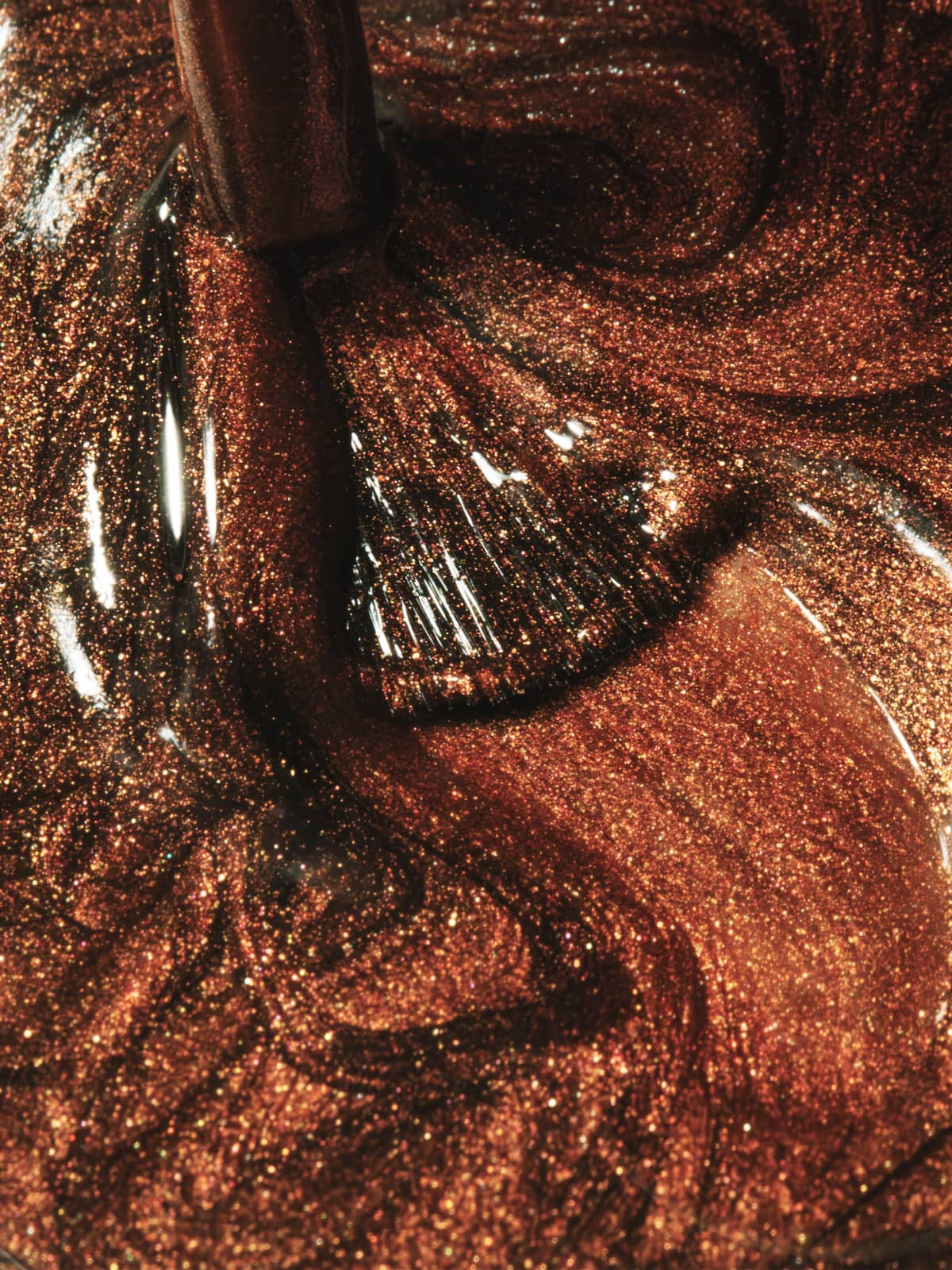 Eine Nahaufnahme eines Pinsels, der durch „Gitti Nr. 218“ – einen metallisch schokoladenbraunen Glitzer-Nagellack – wirbelt, wodurch reflektierende Muster in der dickflüssigen Masse entstehen und dessen intensive Tiefe sowie sein auffälliges Metallic-Finish hervorgehoben werden.