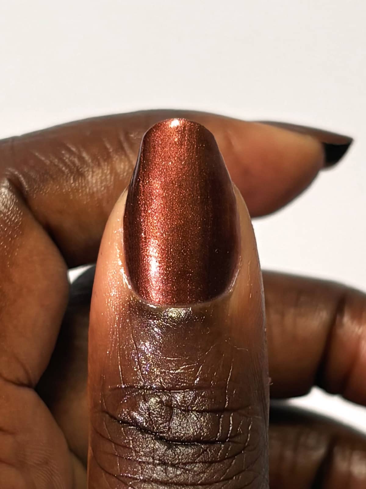 Eine Nahaufnahme eines Daumens, der mit dem Nagellack „Gitti Nr. 218“ lackiert ist. Vor einem schlichten weißen Hintergrund kommen die intensive Tiefe und die dezenten schokoladenbraunen Nuancen des metallisch-kupferfarbenen Tons besonders gut zur Geltung.