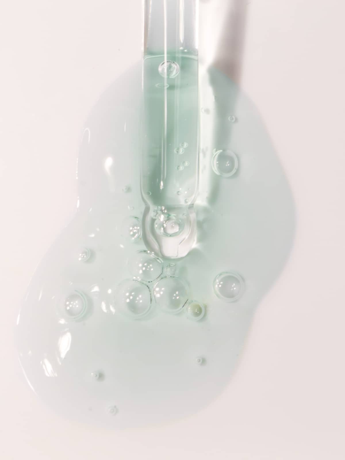 Aus einer Pipette tropft ein klares, hellblaues, mit Bläschen durchsetztes „Aloe Drop Nail Concentrate“ auf eine weiße Oberfläche – ideal zur Pflege der Nagelhaut und für schöne, gesunde Nägel.