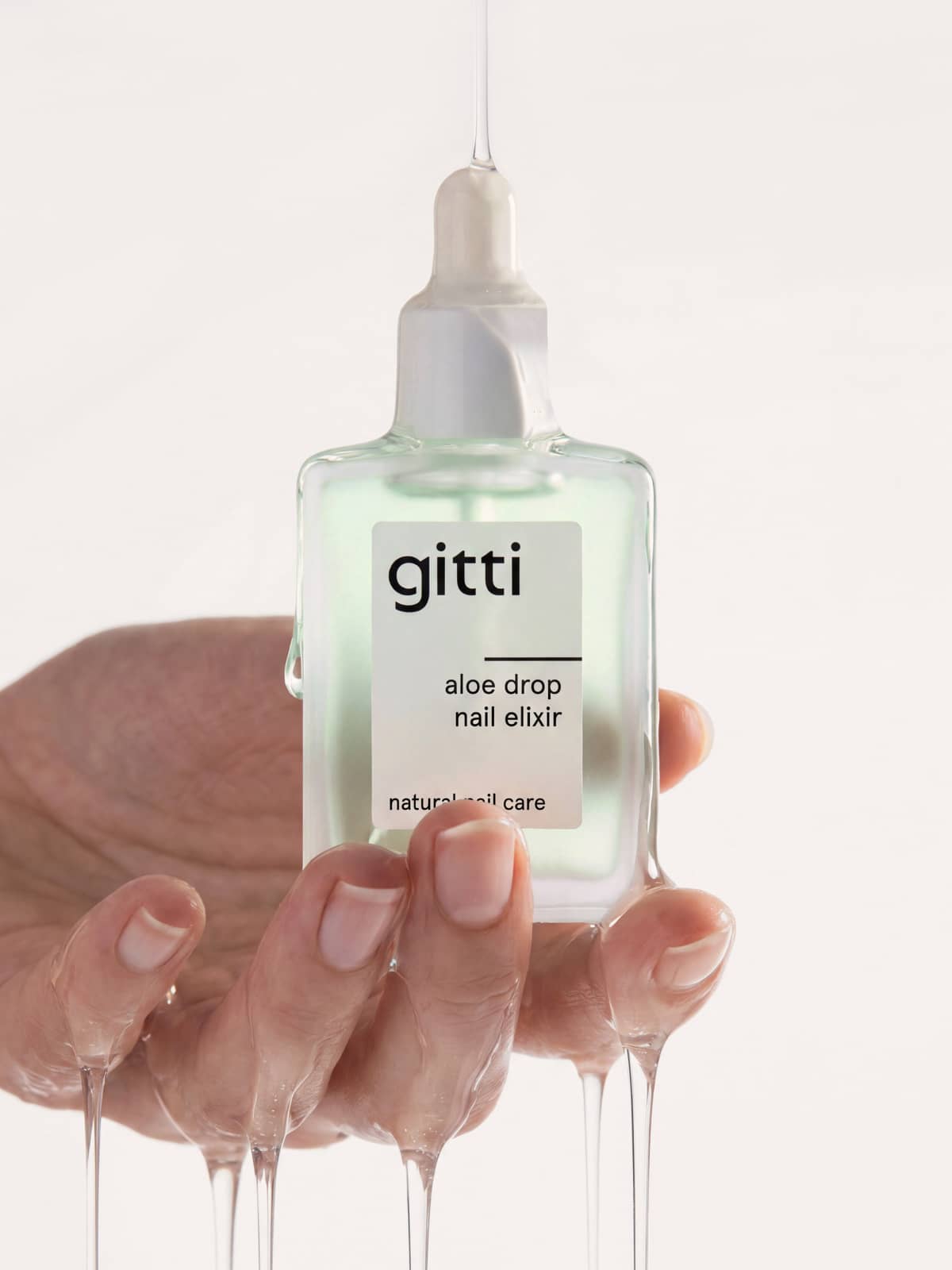 Eine Hand hält eine Glas-Tropfflasche mit der Aufschrift „Aloe Drop Nail Concentrate“, wobei Flüssigkeit sowohl aus der Tropfflasche als auch von der Hand tropft, was die pflegende Wirkung dieses Gel-Serums für Nägel und Nagelhaut unterstreicht.