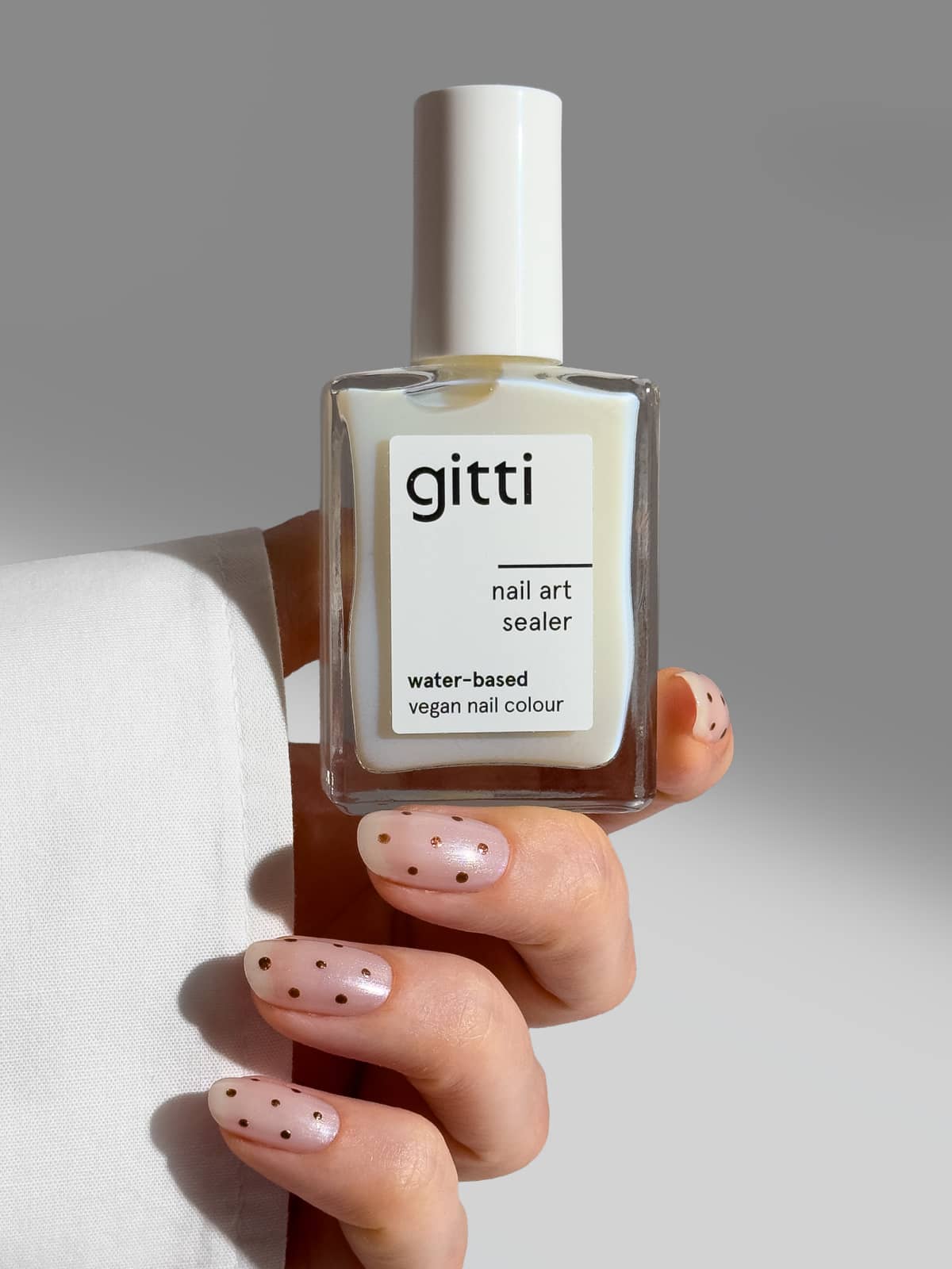 Vor einem neutralen Hintergrund hält eine Hand mit Polka-Dot-Nageldesign eine Flasche „Nail Art Sealer“ in der Hand, die als „wasserbasiert“ und „vegan“ gekennzeichnet ist und das Design perfekt schützt.