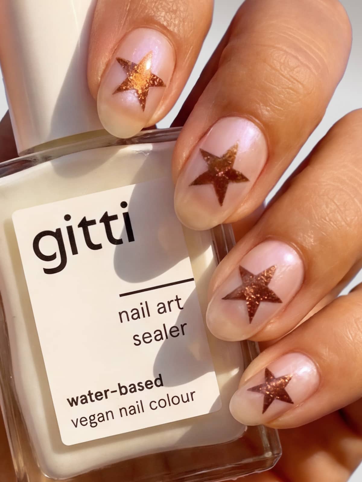 Eine Hand mit glänzenden Nägeln und metallischen Sternmotiven hält eine Flasche mit der Aufschrift „Nail Art Sealer – wasserbasiert, schützt das Design“ – ideal zum Versiegeln Ihres veganen Nagellacks auf Wasserbasis.