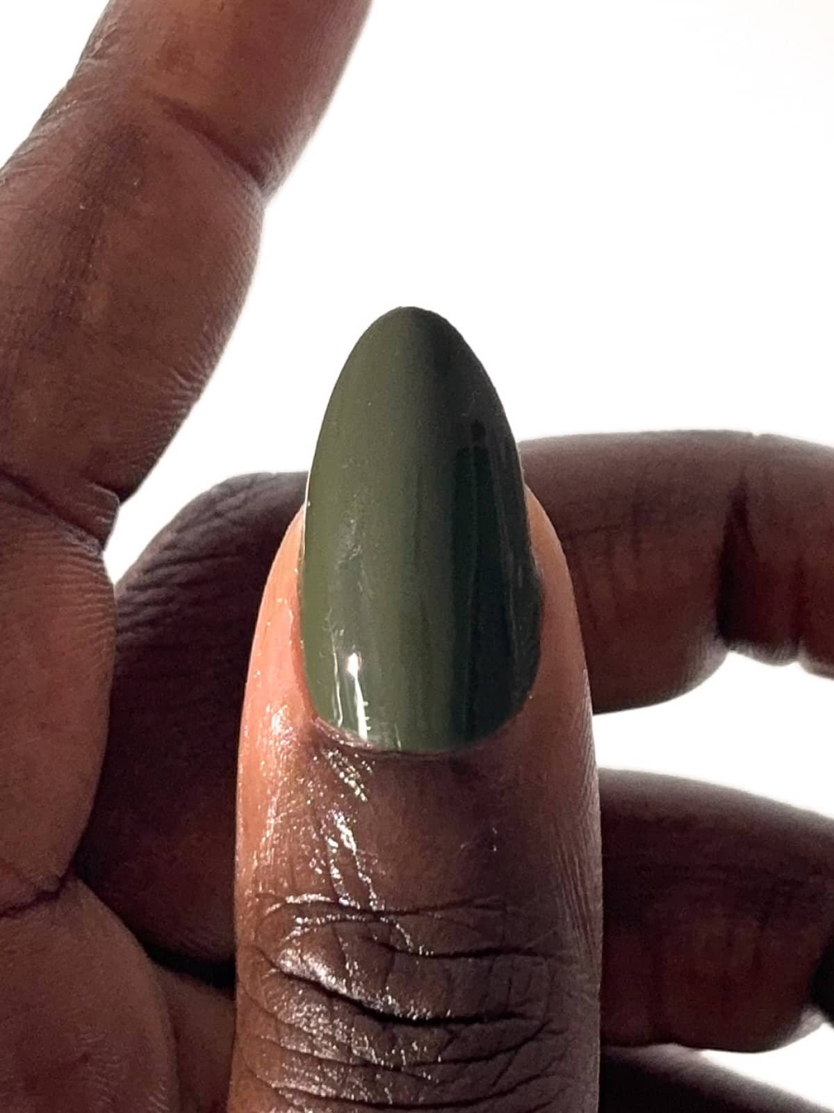 Eine Nahaufnahme einer Hand, auf der der Daumen mit dem glänzenden Nagellack „Gitti Nr. 061“ in einem dunklen Olivgrün vor einem schlichten weißen Hintergrund zu sehen ist.