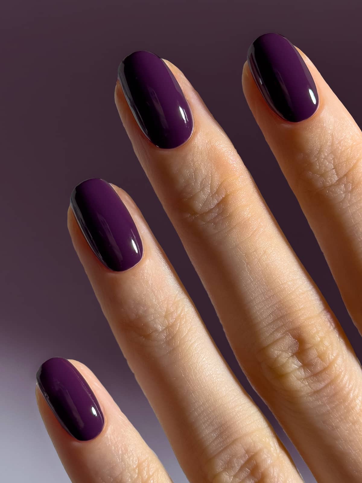 Eine Nahaufnahme einer Hand, auf der vier Finger zu sehen sind, deren Nägel jeweils mit dem glänzenden Nagellack „Gitti Nr. 062“ mit einem rötlichen Unterton lackiert sind, vor einem violetten Hintergrund.
