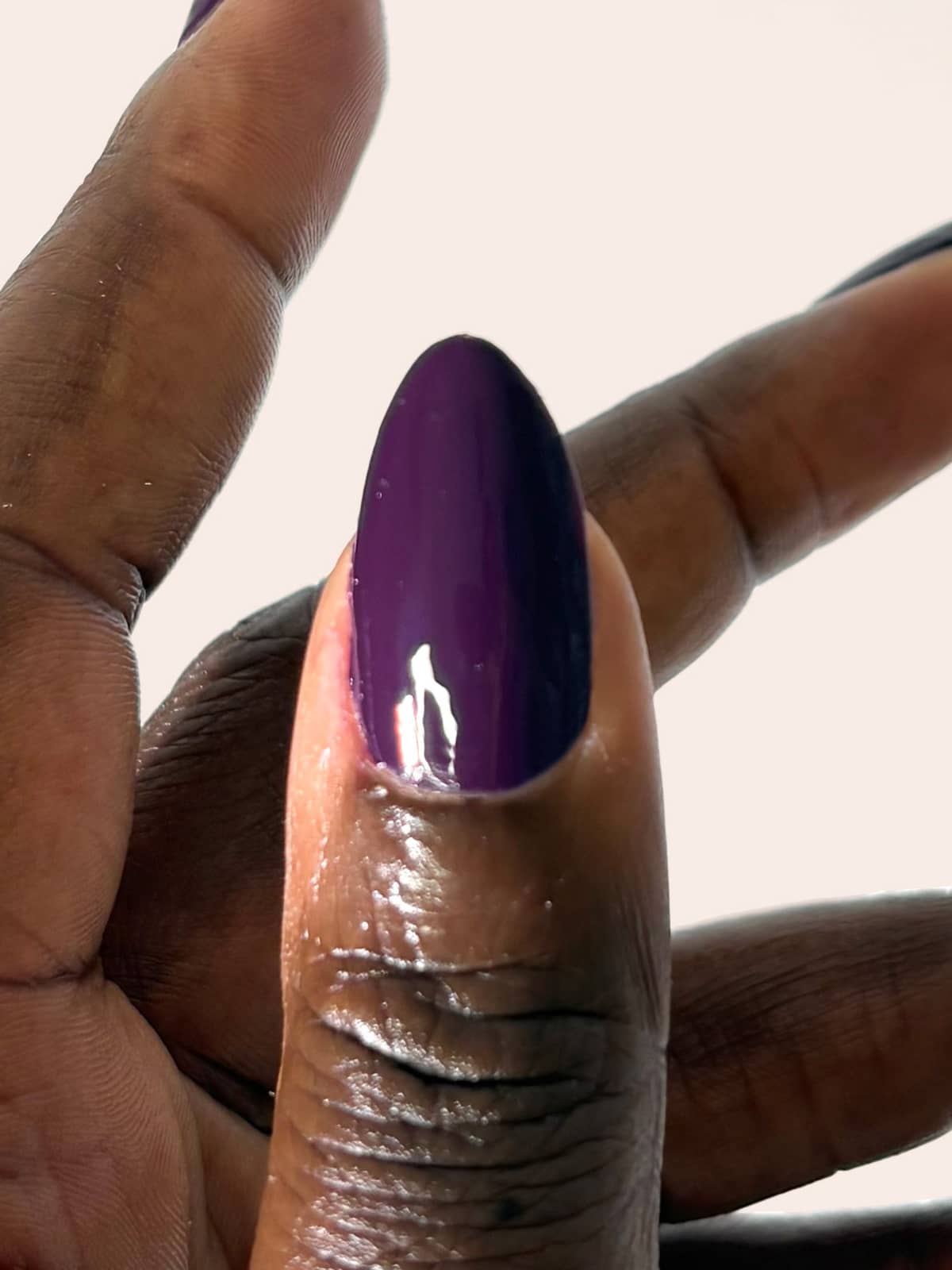 Eine Nahaufnahme einer Hand mit dunkler Haut, auf der der Daumennagel mit dem glänzenden Nagellack „Gitti Nr. 062“ lackiert ist, der einen dezenten rötlichen Unterton aufweist, vor weißem Hintergrund.